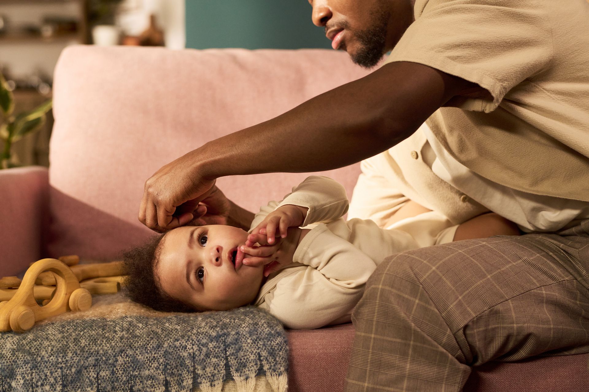 Adult gently tending to a baby on a couch with pink pillows and a blanket