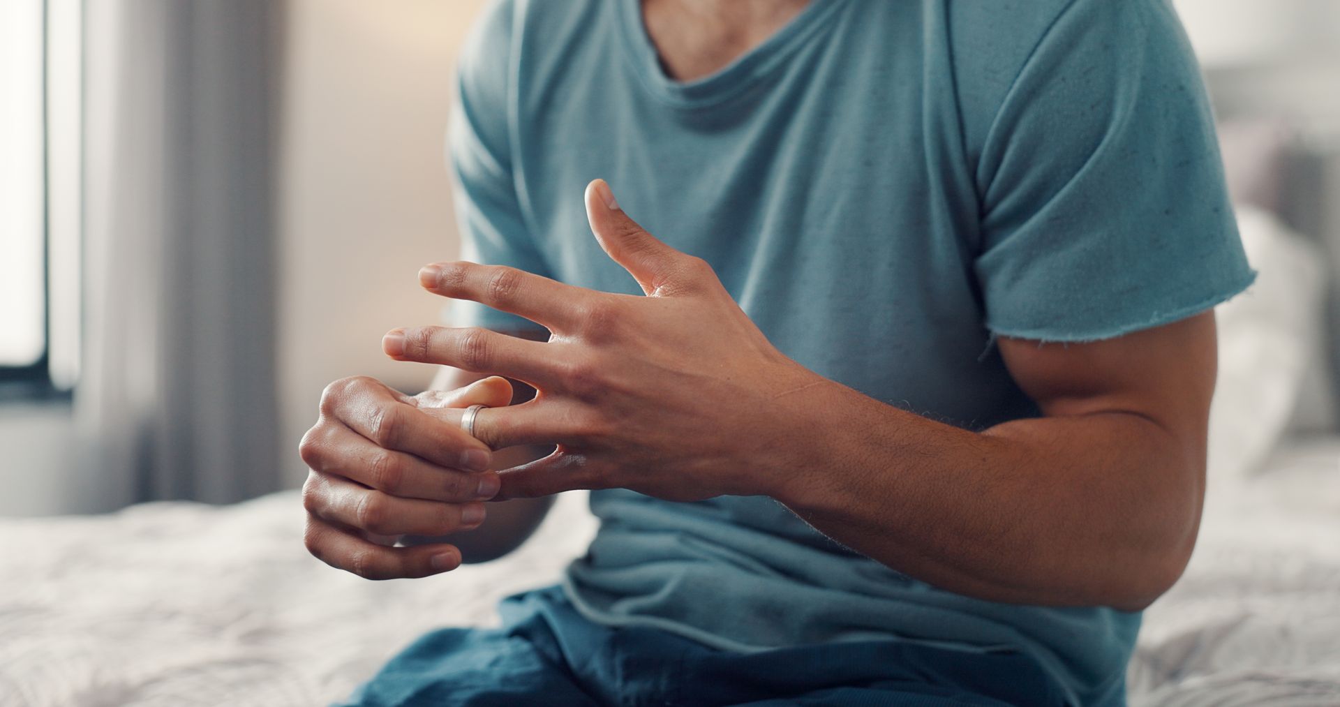 a man sitting on a bed and removing his wedding ring