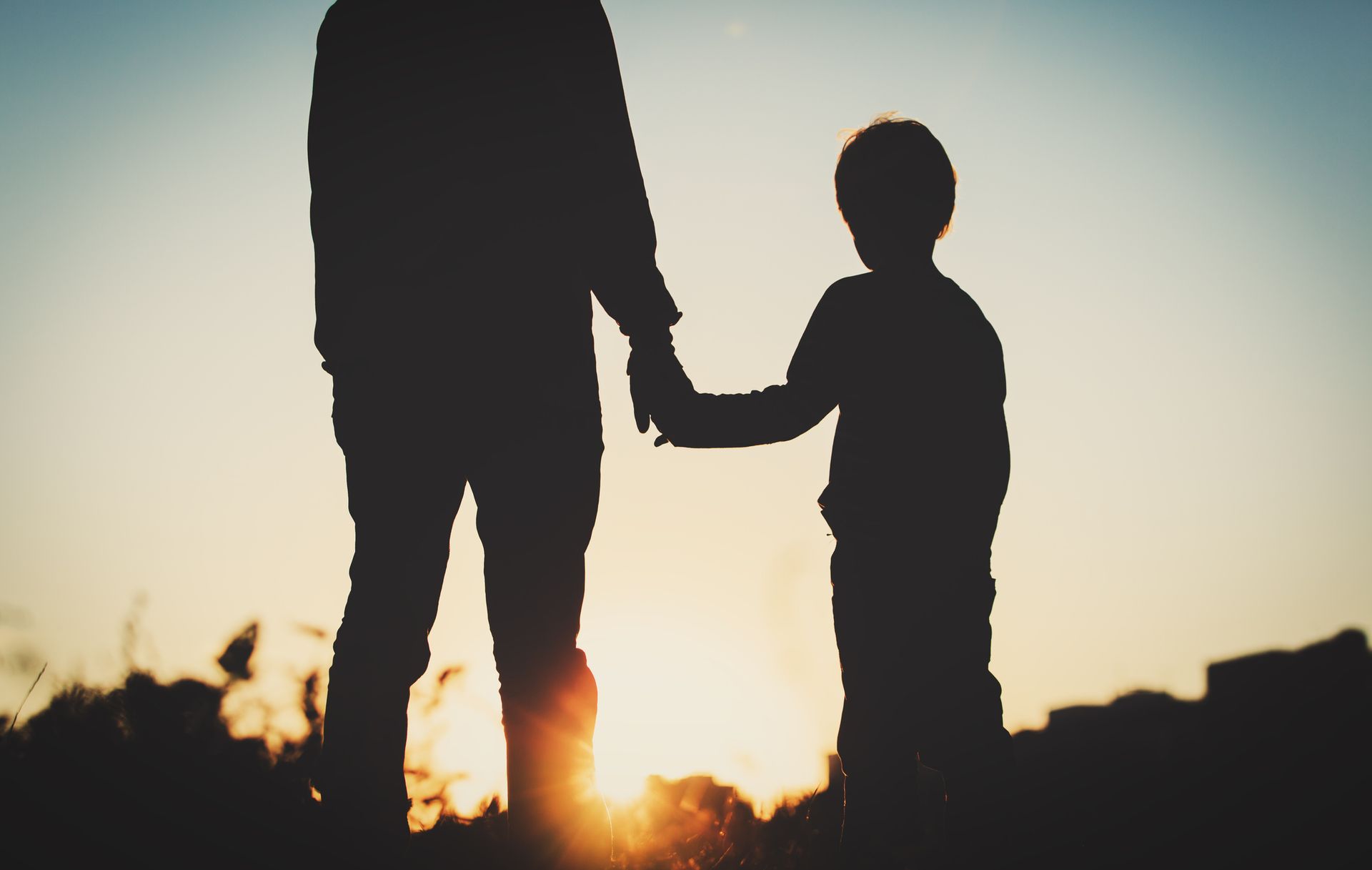 a silhouette of a parent with their child in front of a sunset