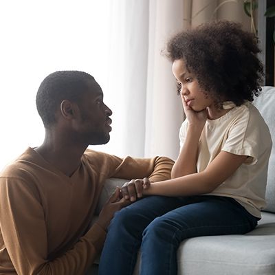 A father and his daughter are sitting on a couch talking to each other.