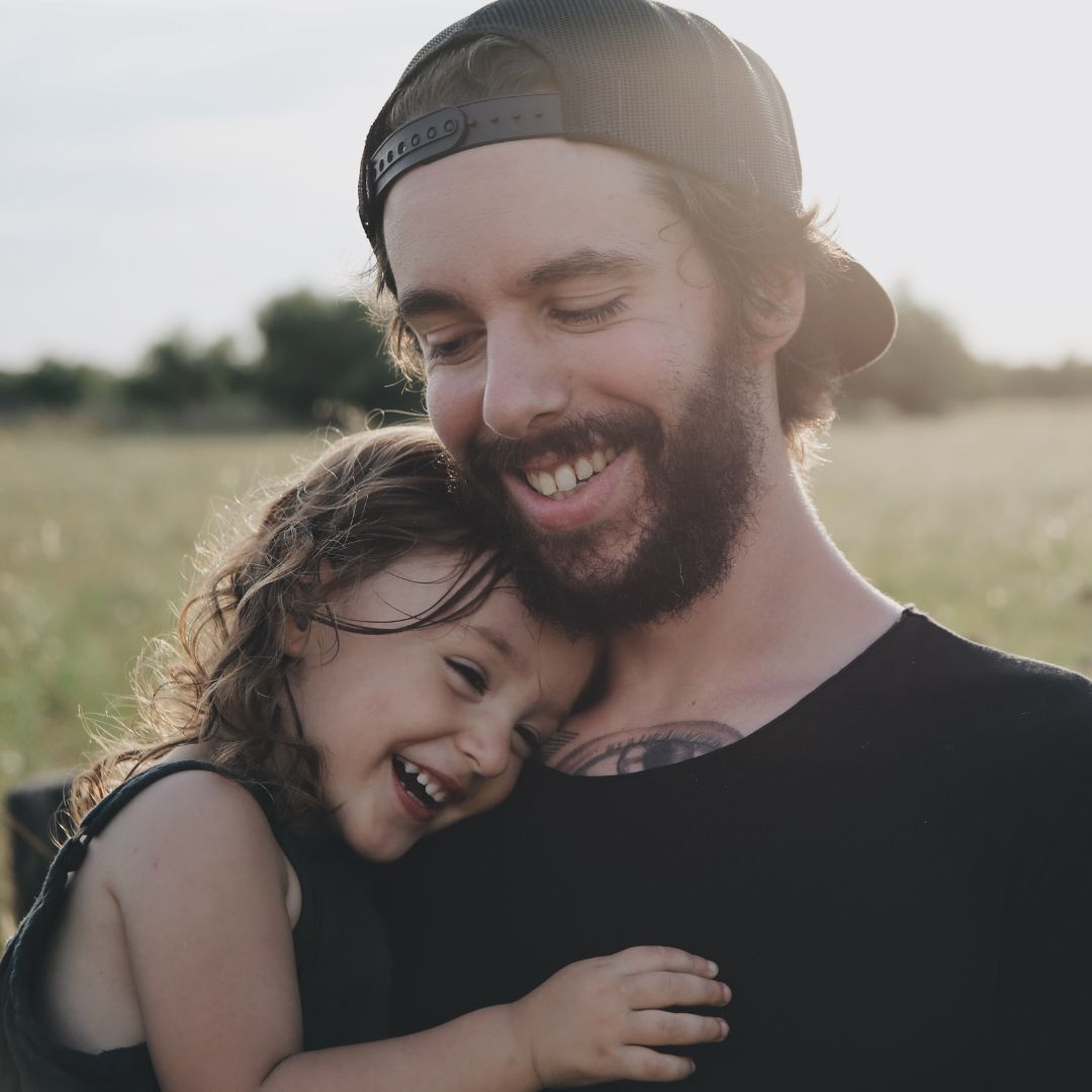 A man with a beard is holding a little girl in his arms.