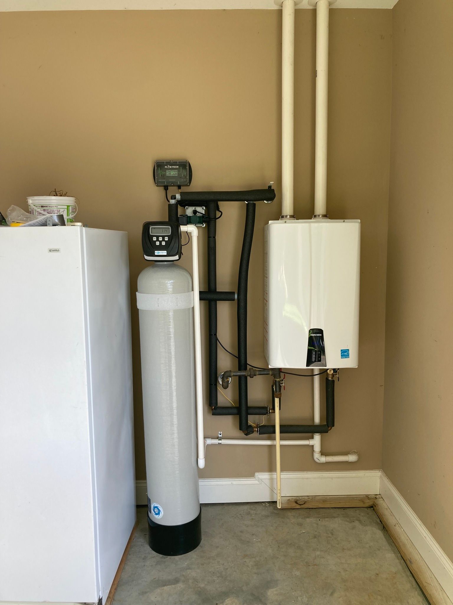 Water softener and tankless water heater in a garage, next to a white refrigerator.