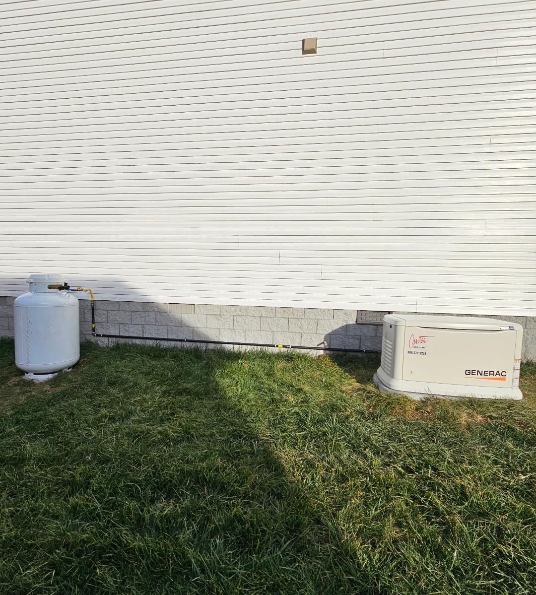A propane tank and generator sit on grass next to a white-walled building.