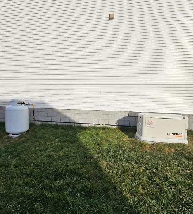 Black gas pipes run along a brick wall and connect to a beige generator unit.