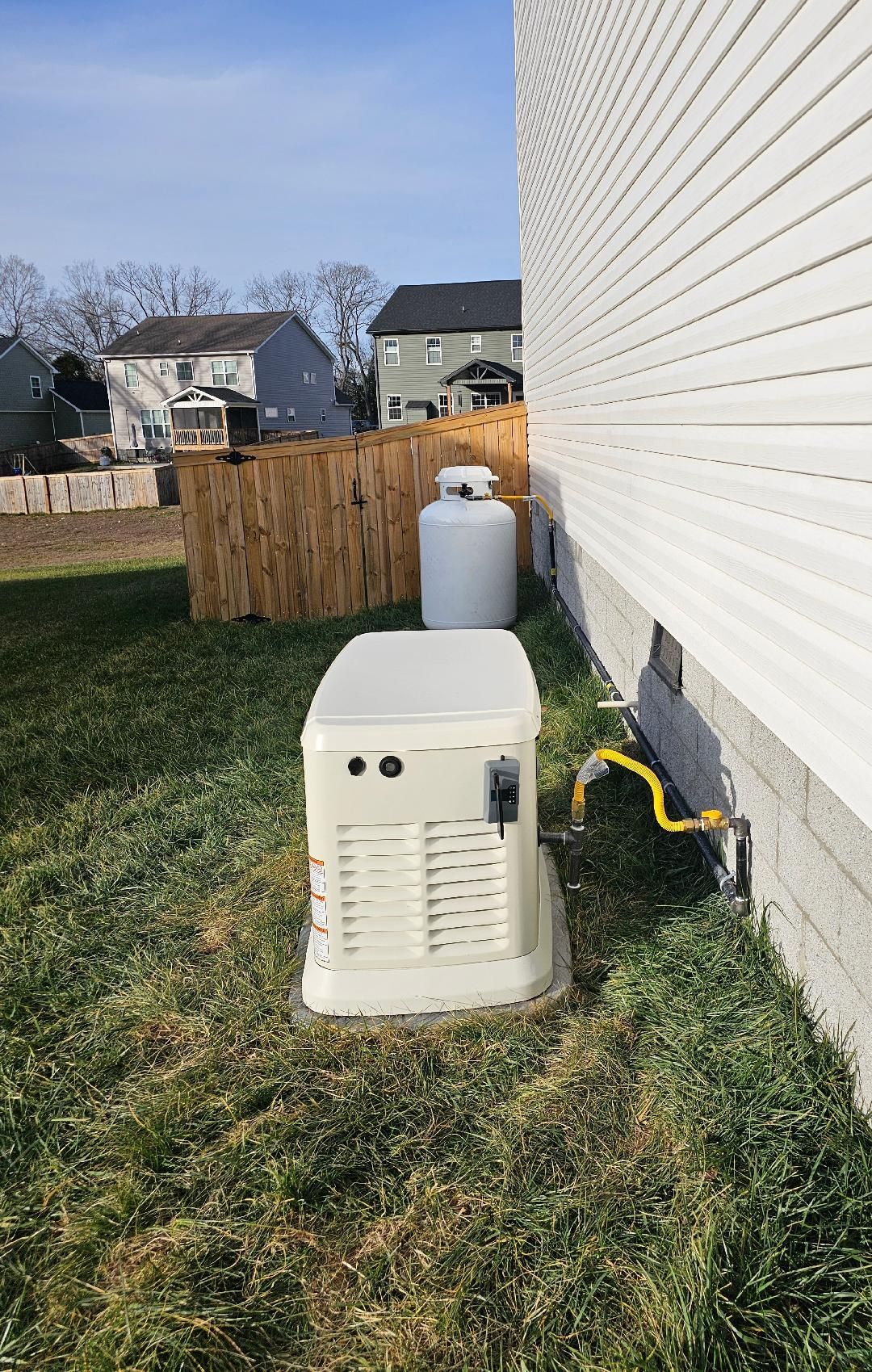 Generator, propane tank, and wooden fence near a house.
