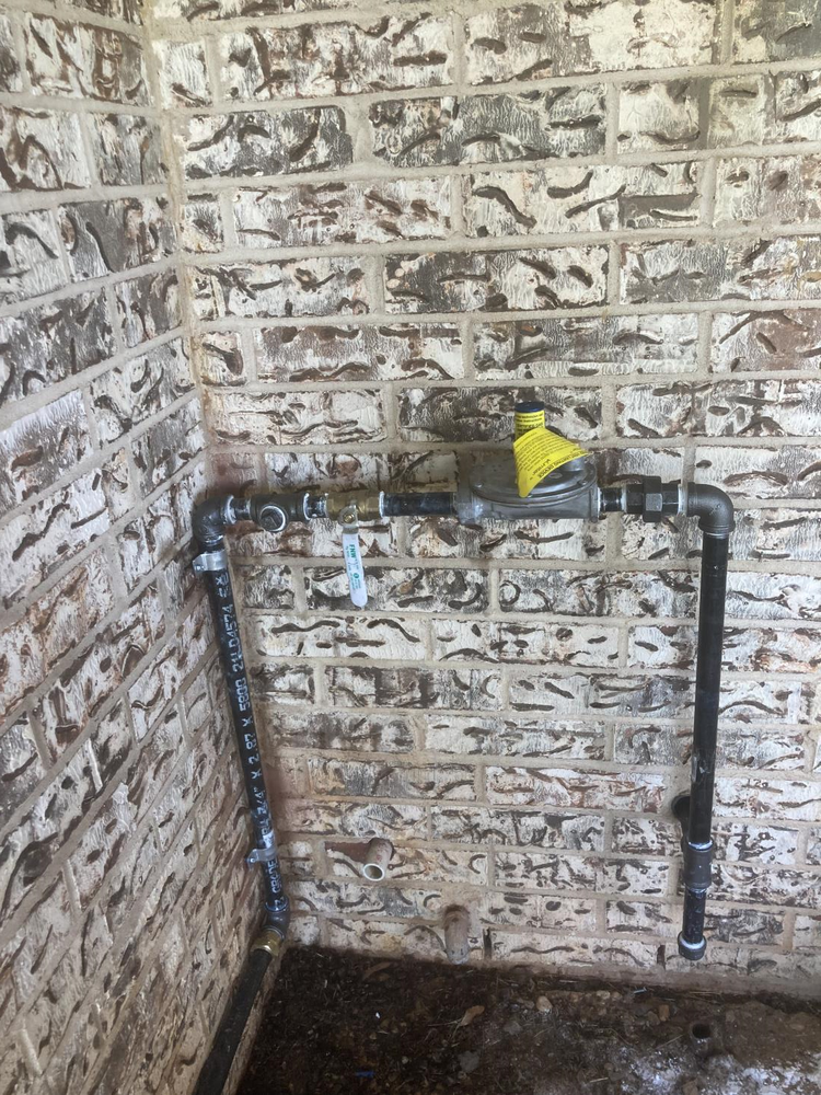Gas meter and pipes mounted on a brick wall, with a yellow cap on top.