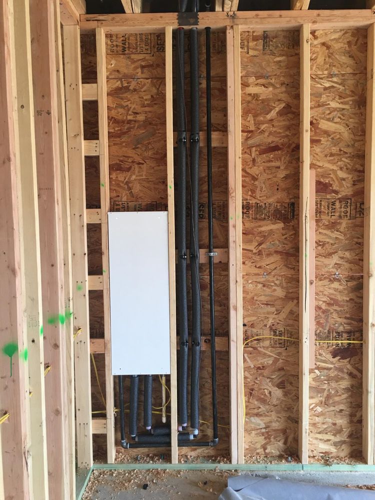 Interior wall under construction with black pipes and a white panel in the center.