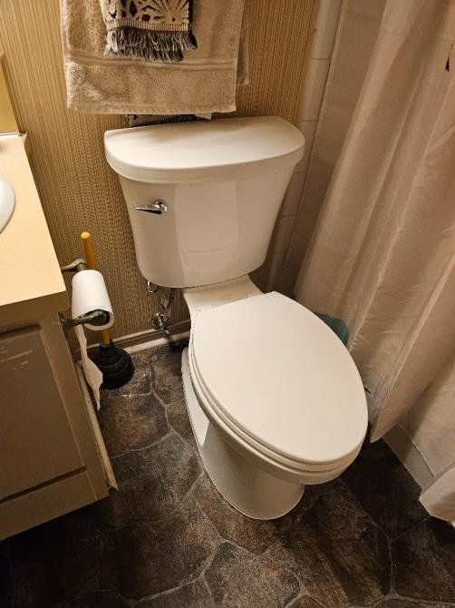 White toilet in a small bathroom with patterned flooring and a shower curtain. A towel hangs above.