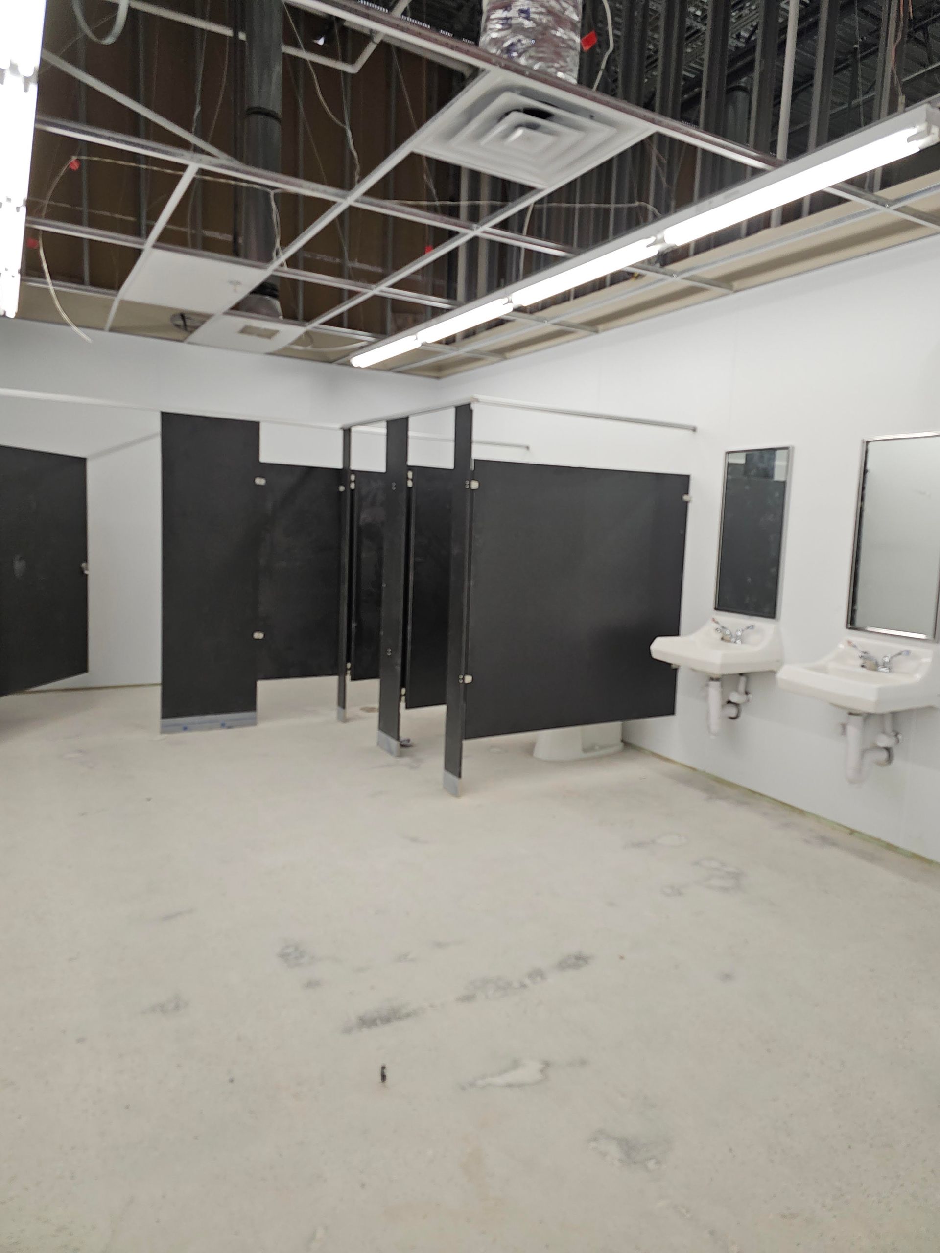 A public restroom under construction with stalls, sinks, and exposed ceiling framework.