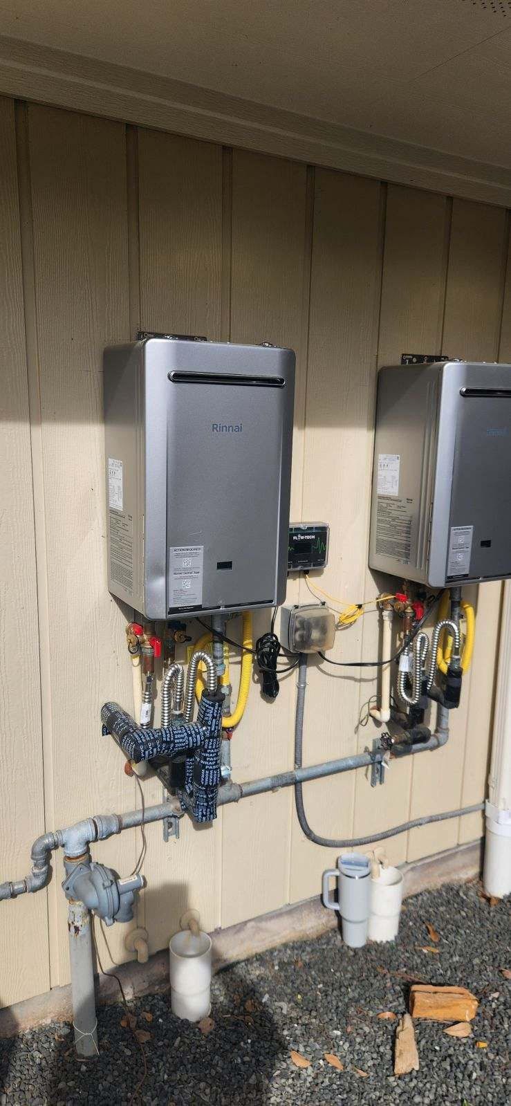 Two outdoor tankless water heaters mounted on a wall with plumbing.