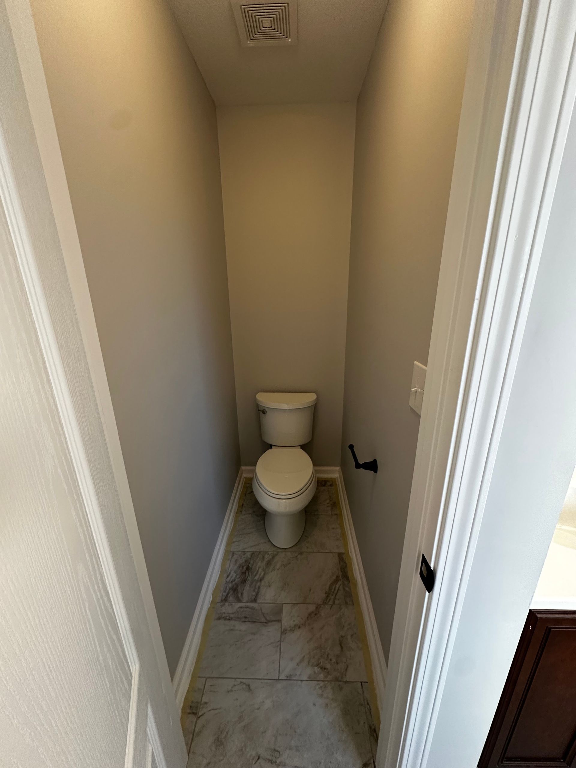 Small bathroom with a toilet, gray walls, and light-colored tile flooring.