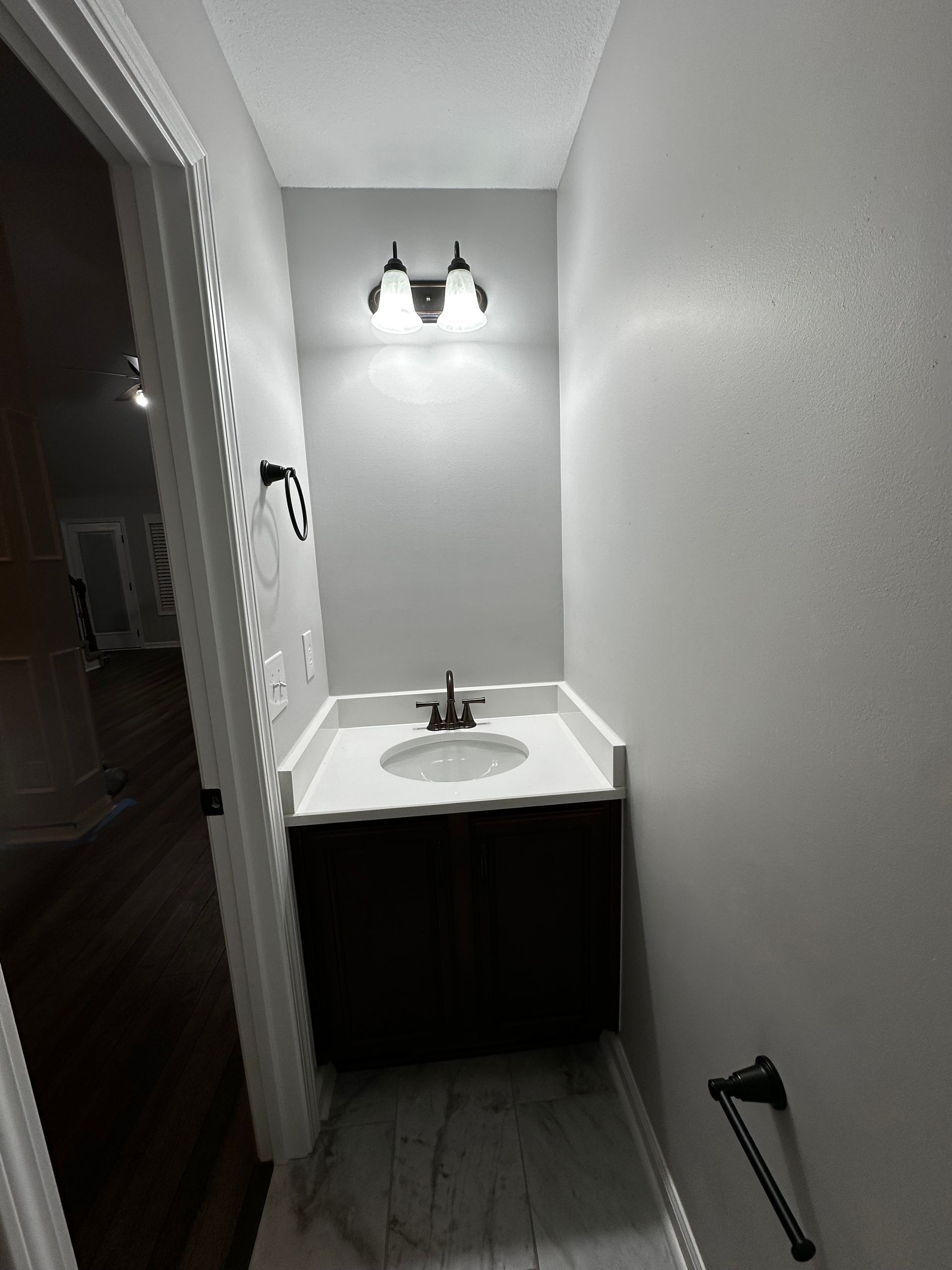 Small bathroom with a dark cabinet, white countertop, and light fixtures.