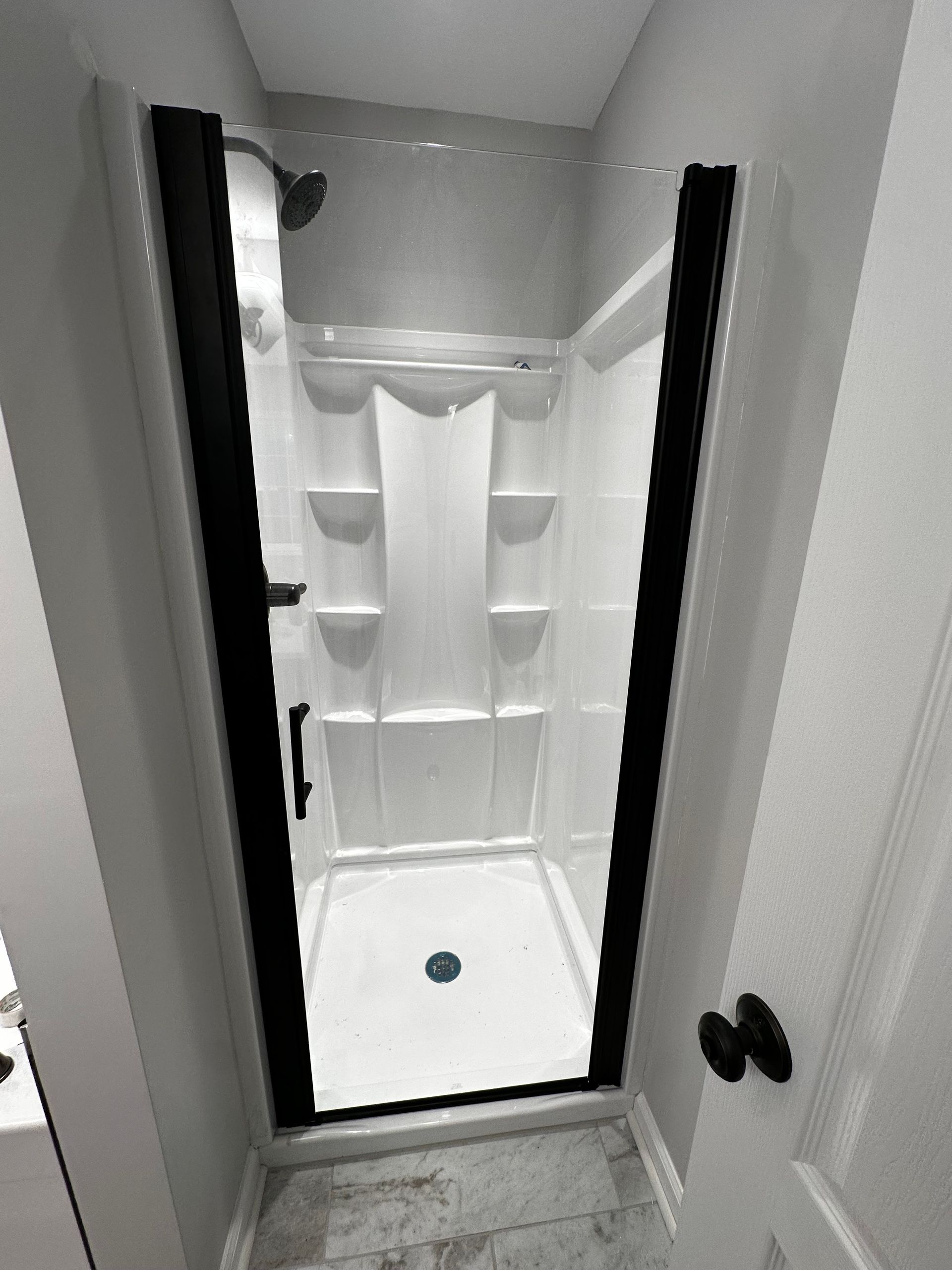 Shower stall with black frame and clear glass door; white interior, shower head, and soap niches.