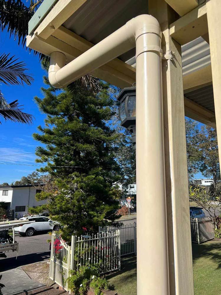 A White Pipe is Hanging From the Side of a House Next to a Tree — Gutterworx in Wamberal, NSW