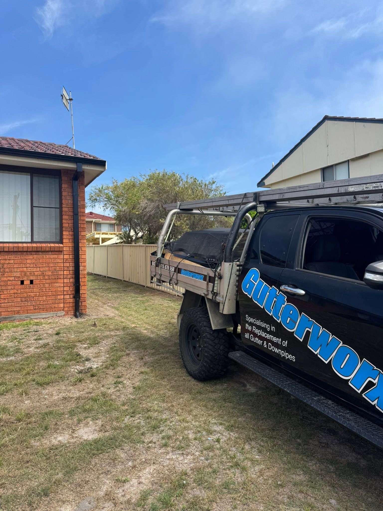 Black off-road truck parked beside a brick house on a grassy yard under a blue sky — Gutterworx In Wamberal NSW