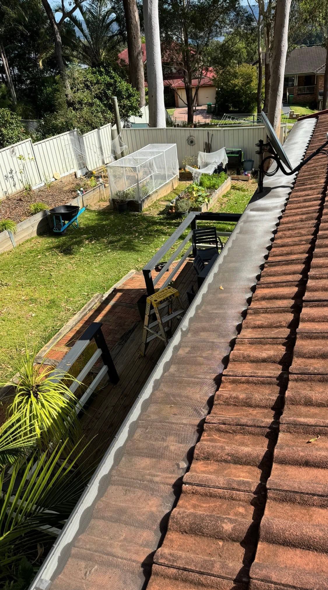 Rooftop garden with terracotta tiles, plants, a white fence, and a bench in the sunlight — Gutterworx in Wamberal, NSW