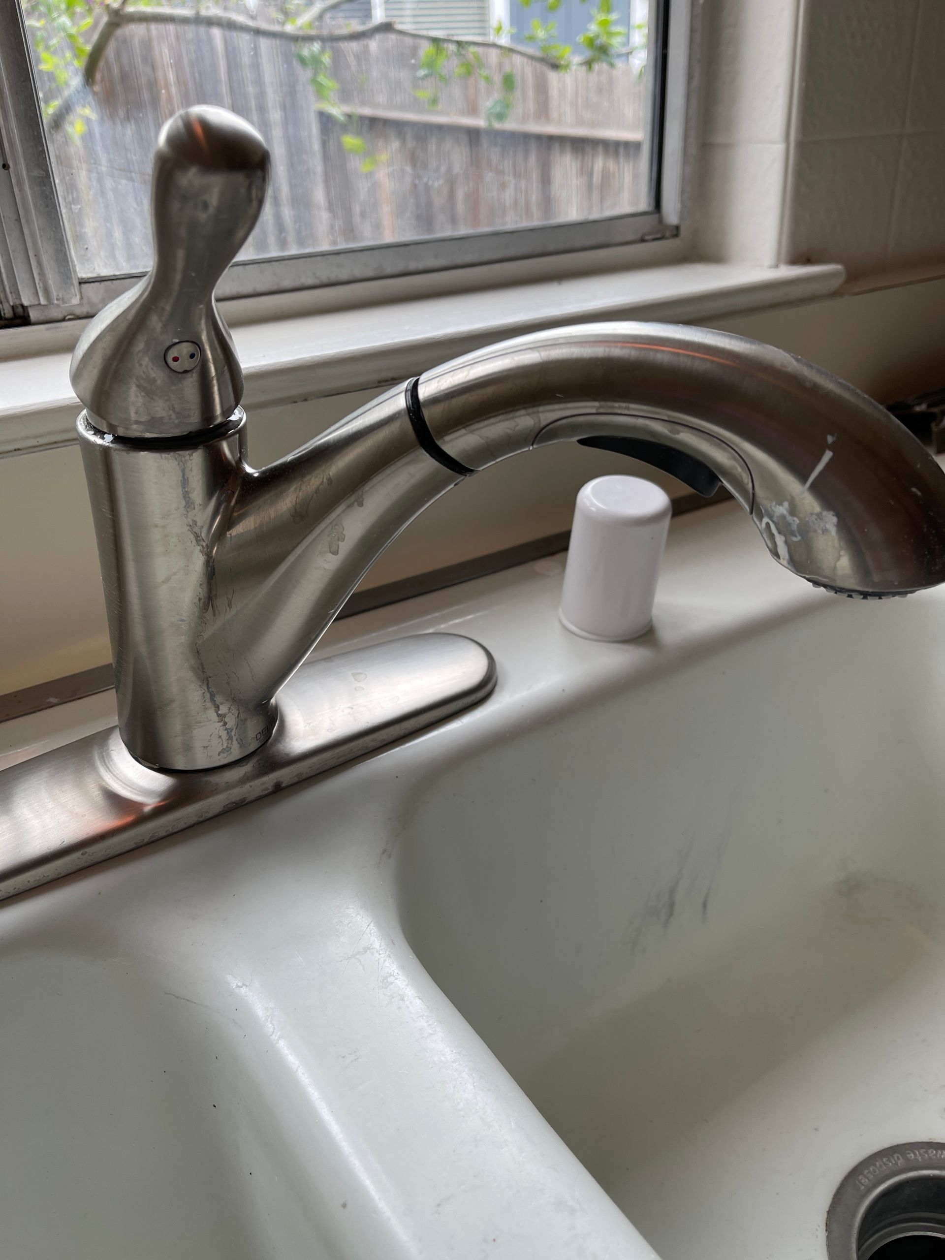 A kitchen sink with a faucet and a window in the background.