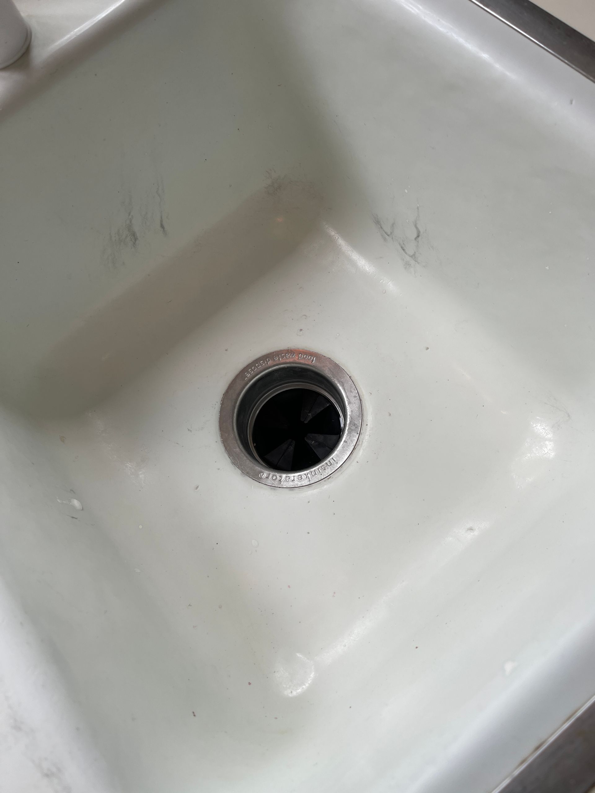 A white kitchen sink with a black hole in the drain.