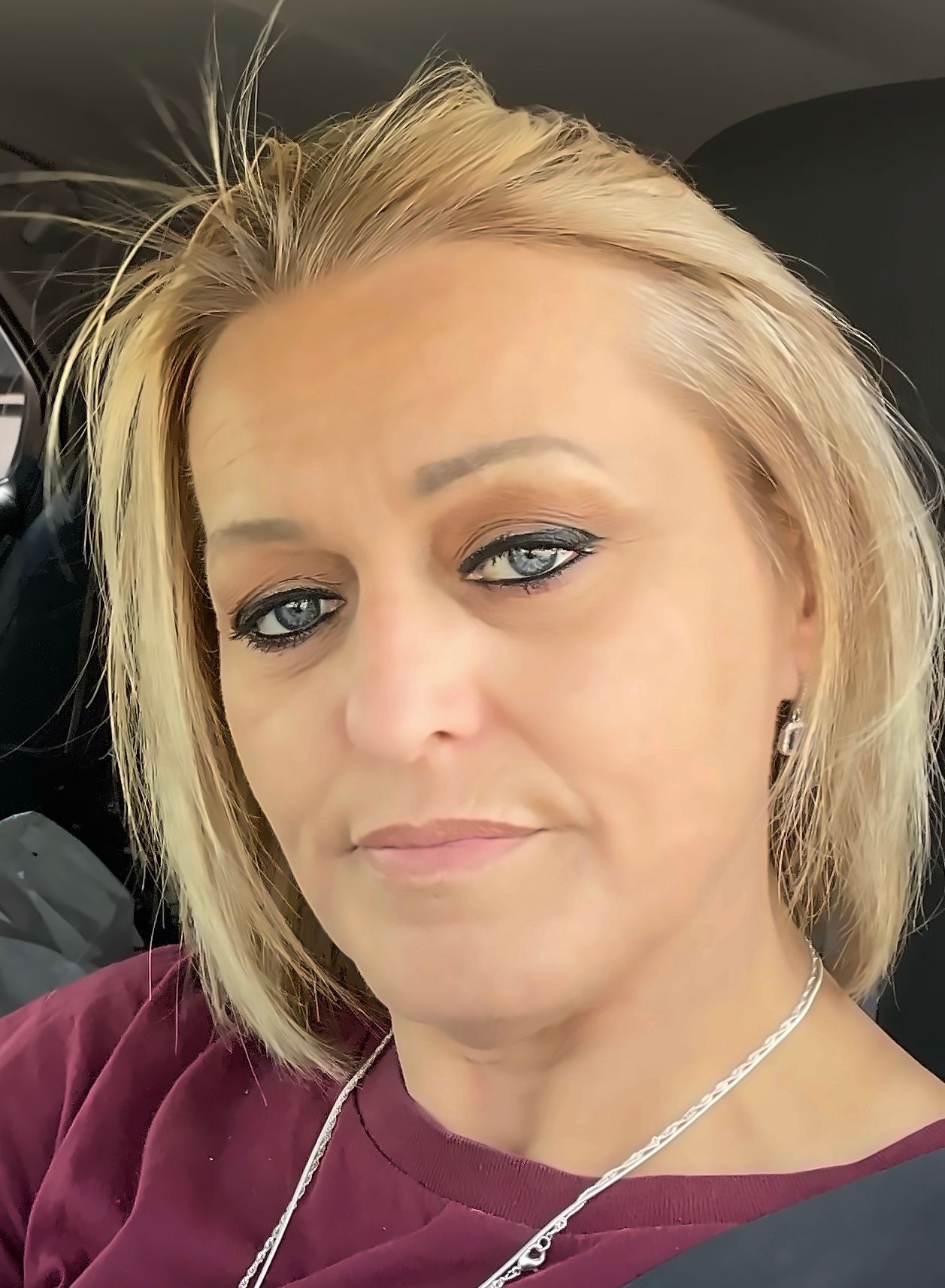 A woman with blonde hair and blue eyes is sitting in a car.