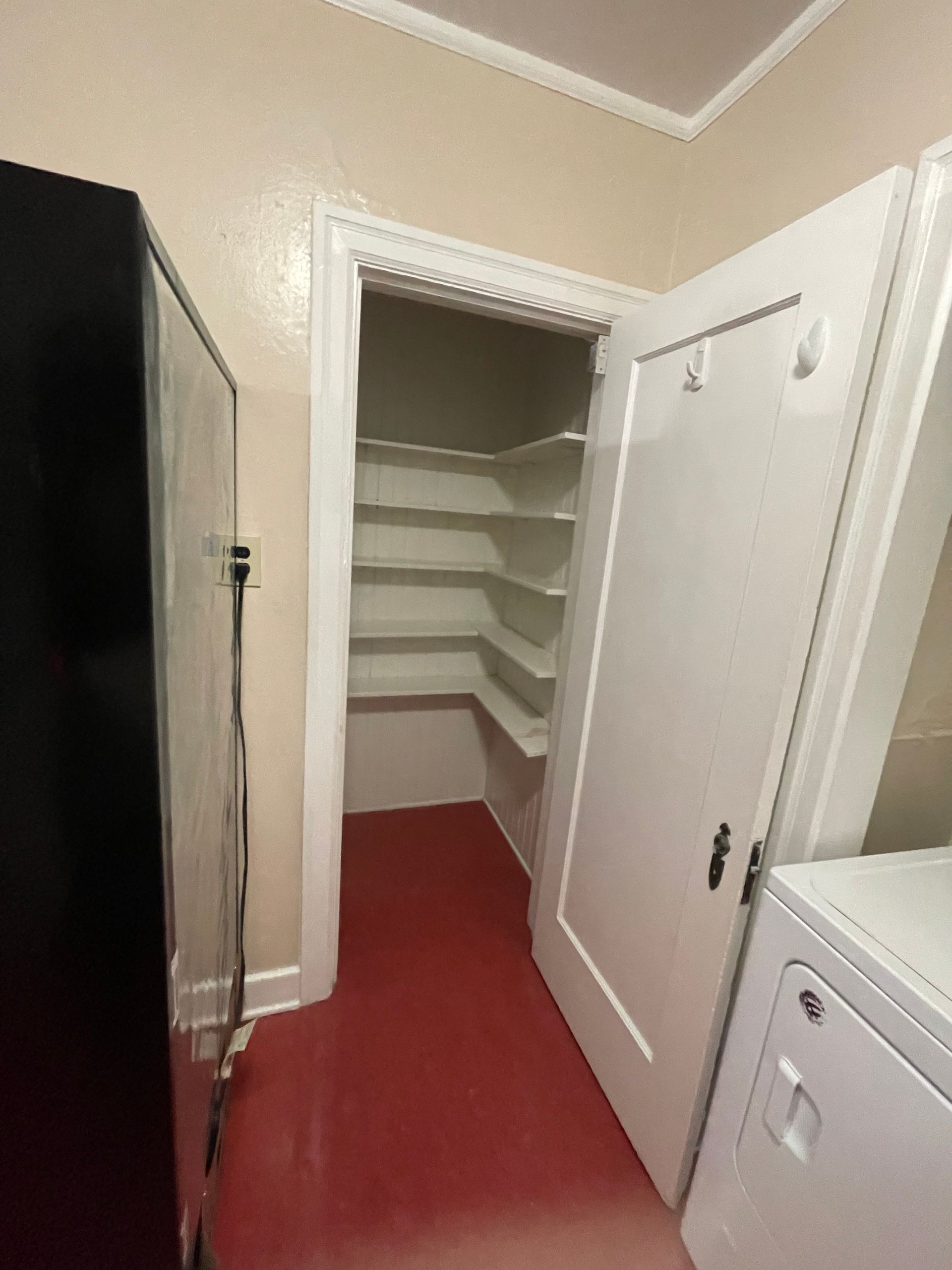 A pantry with white shelves, red floor, and a door next to a white washing machine.