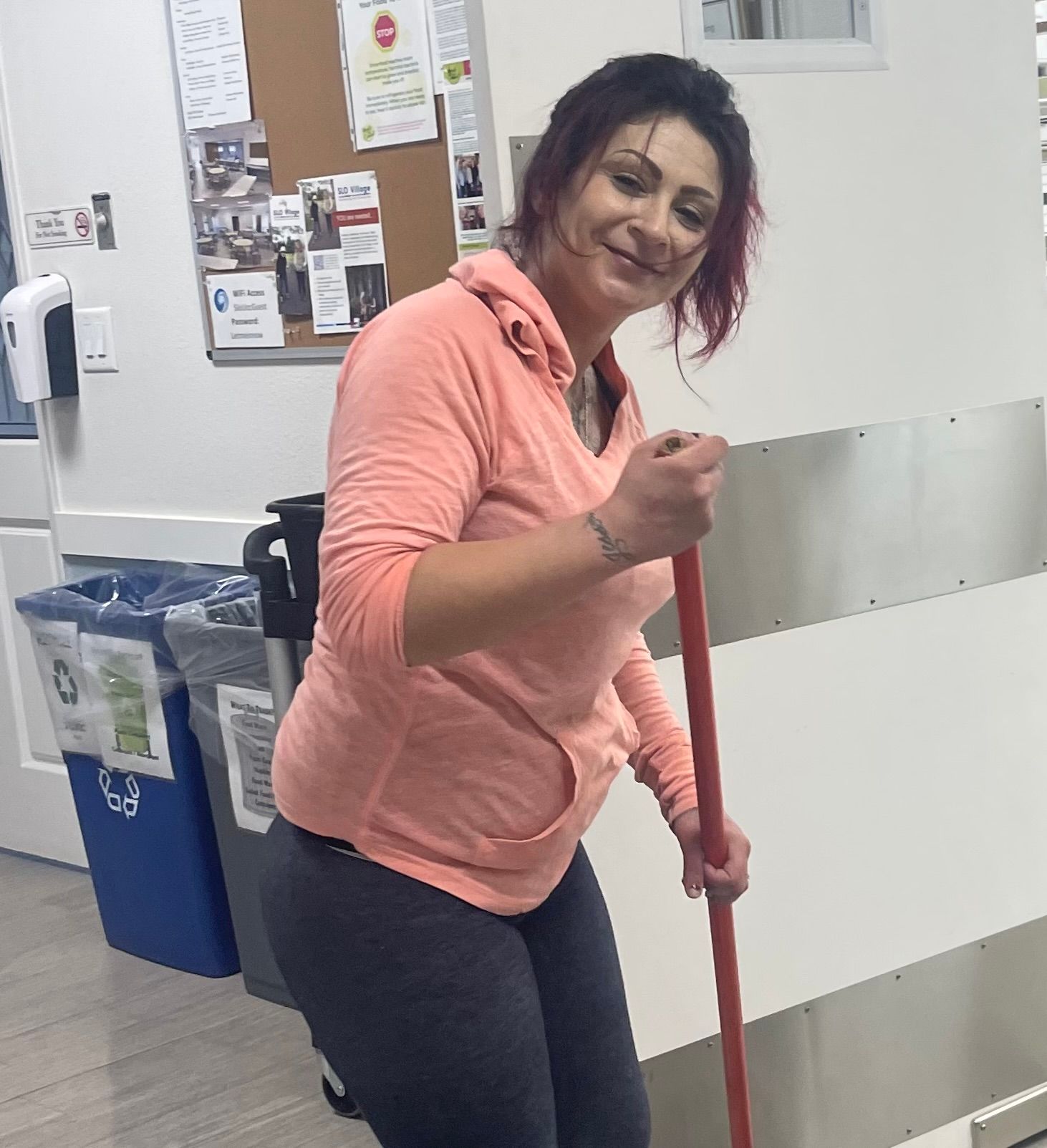 A woman in a pink shirt is holding a red mop