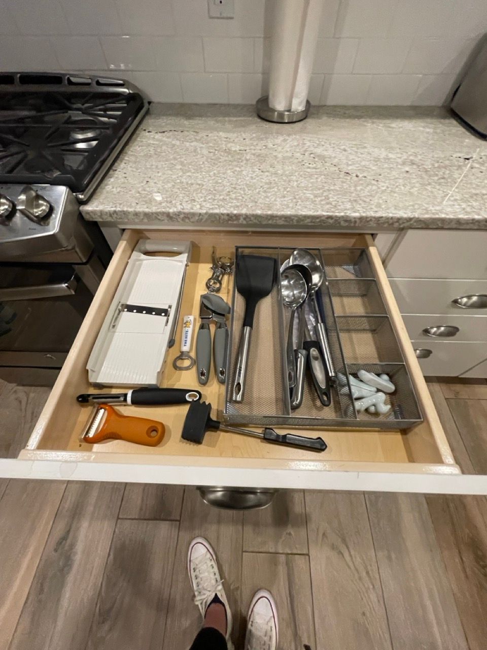 A person is standing next to a kitchen drawer filled with utensils.