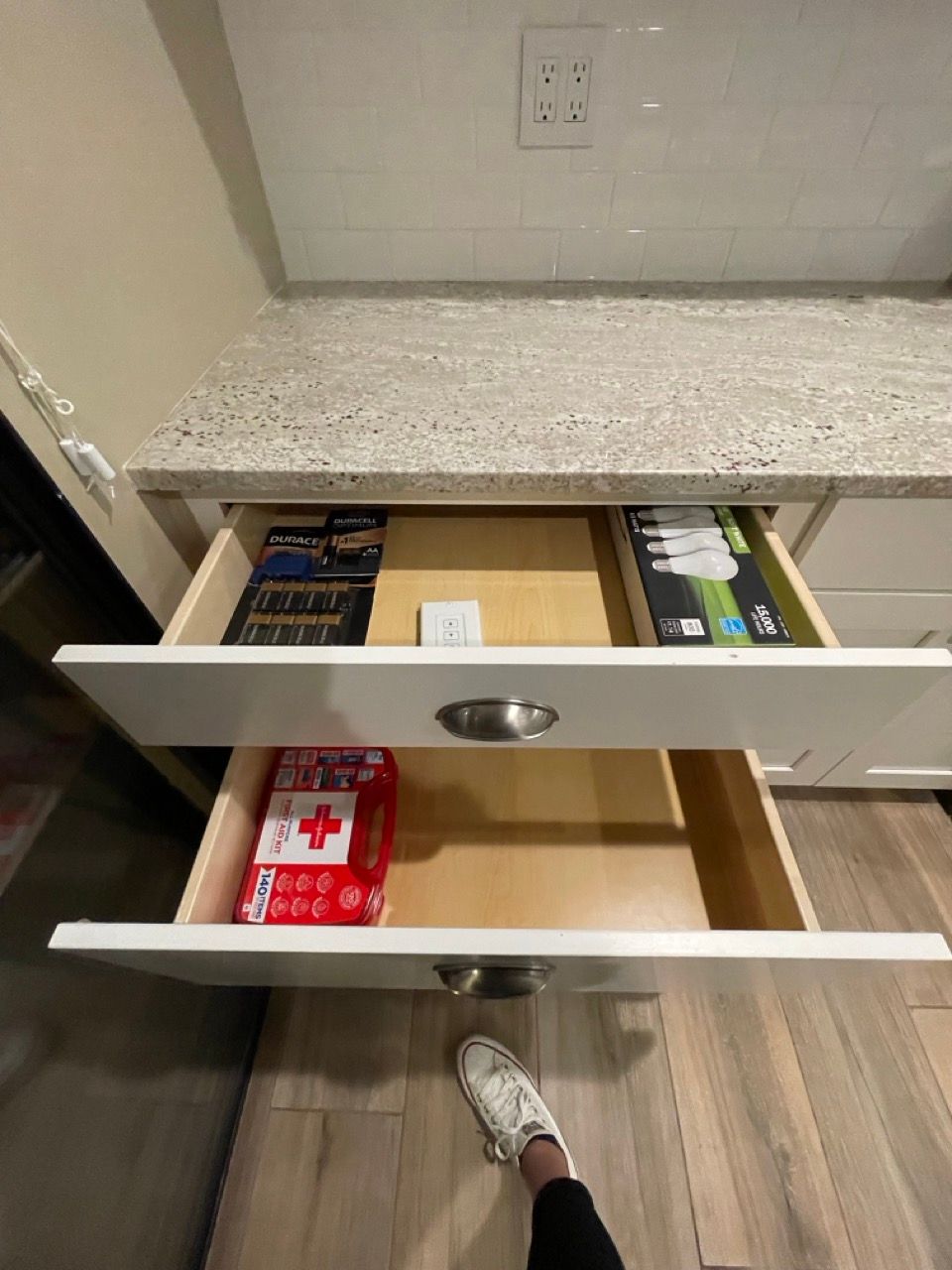 A person is standing next to an open drawer in a kitchen.