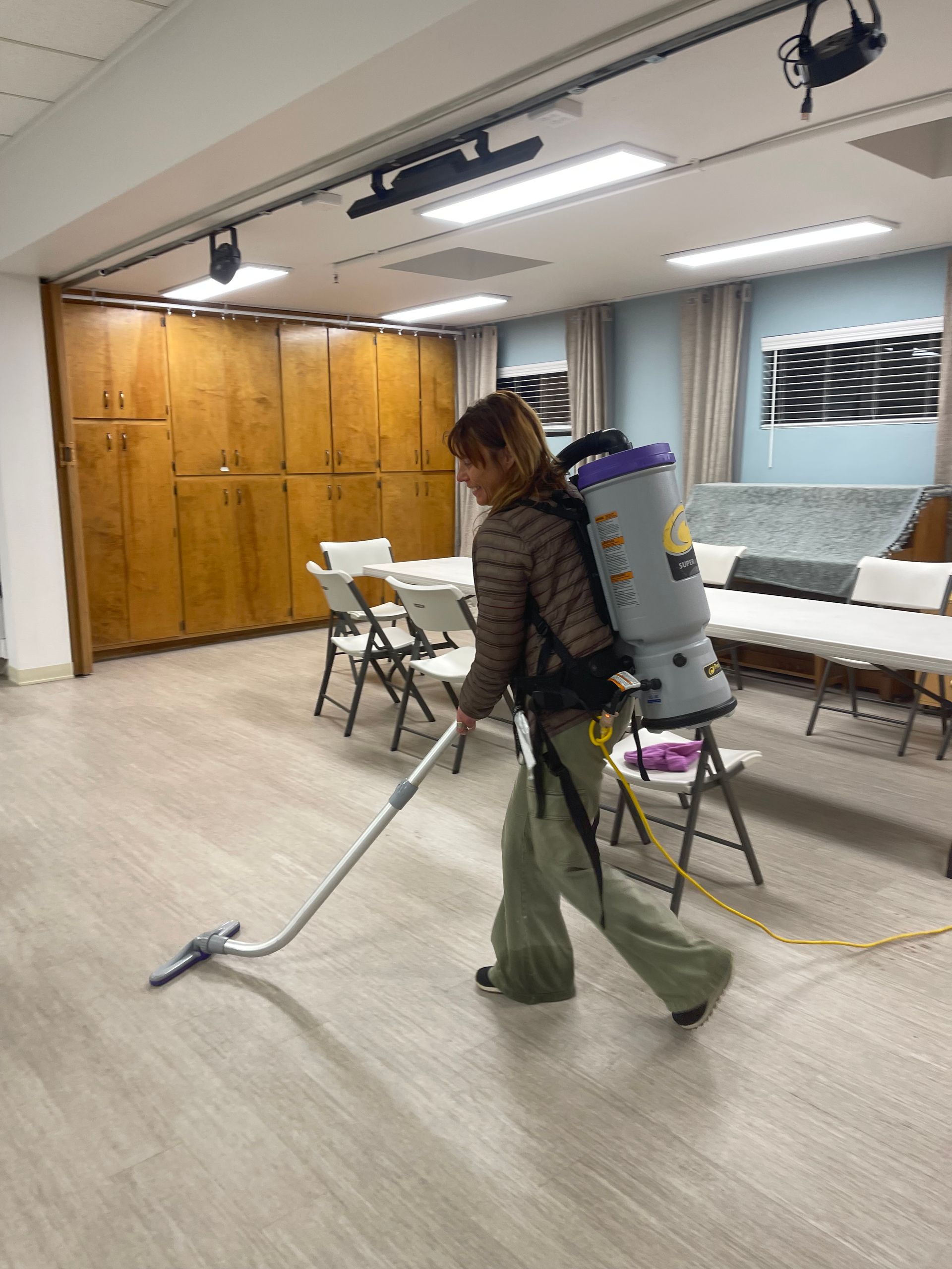 A woman is using a backpack vacuum to clean a room