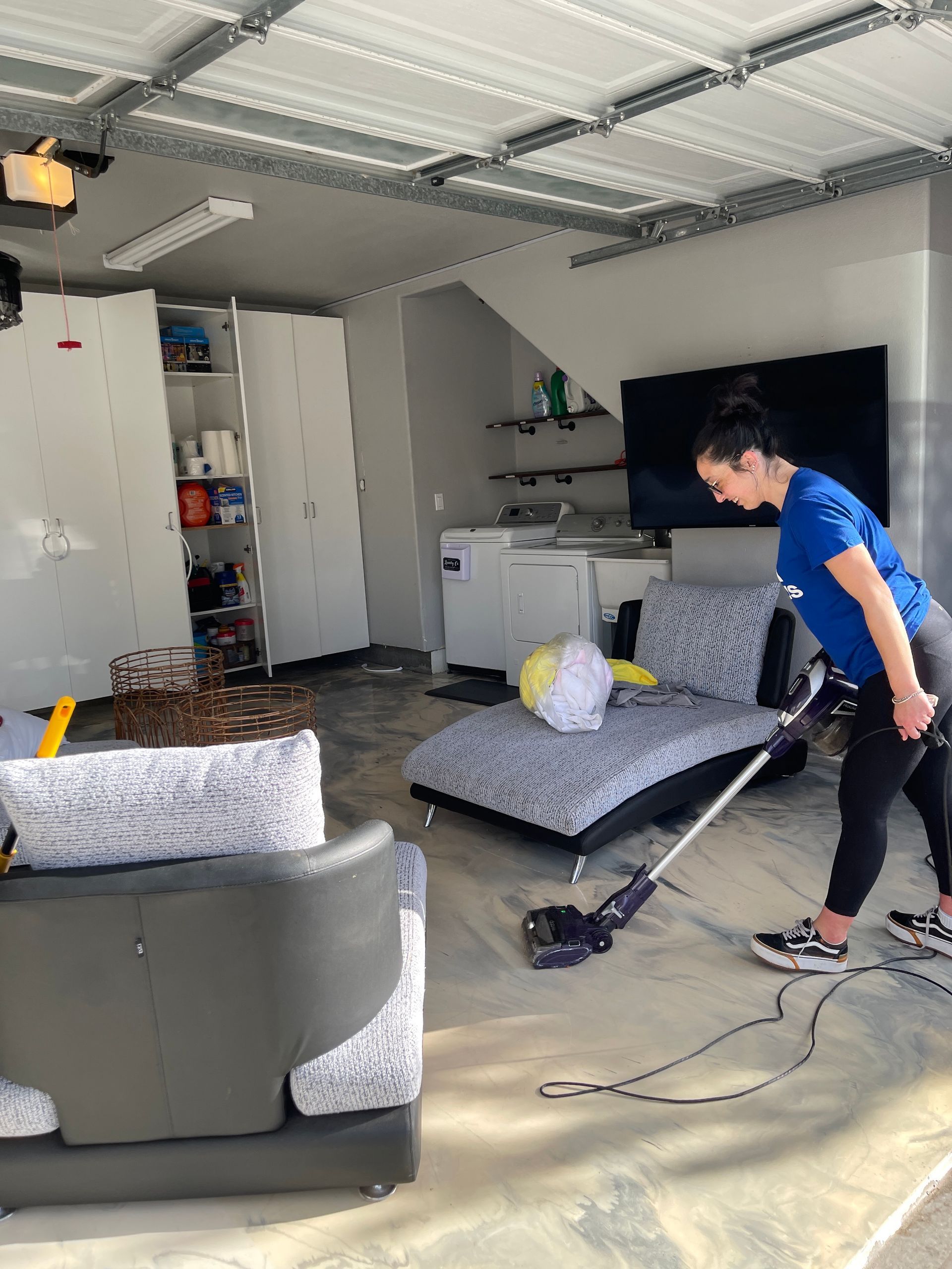 A woman is vacuuming the floor of a living room in a garage.