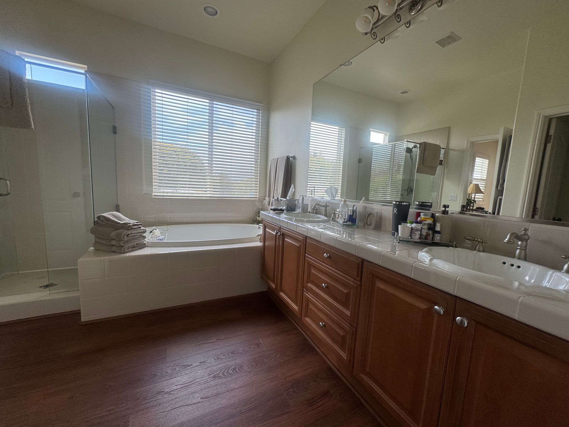 Bathroom with brown cabinets, white countertops, large mirror, bathtub, and shower.