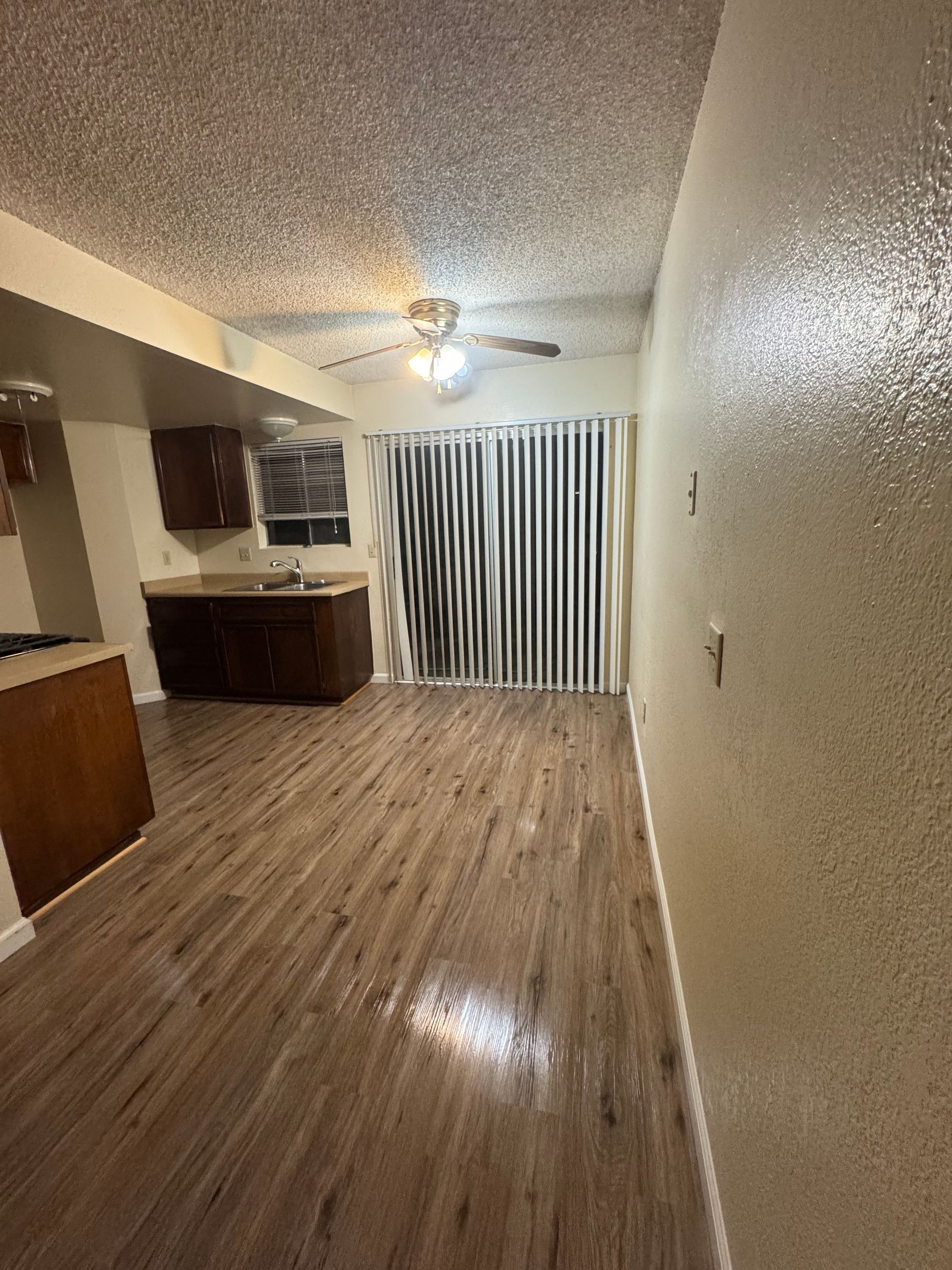 A room with wood floors, kitchen cabinets, sliding door, and ceiling fan.