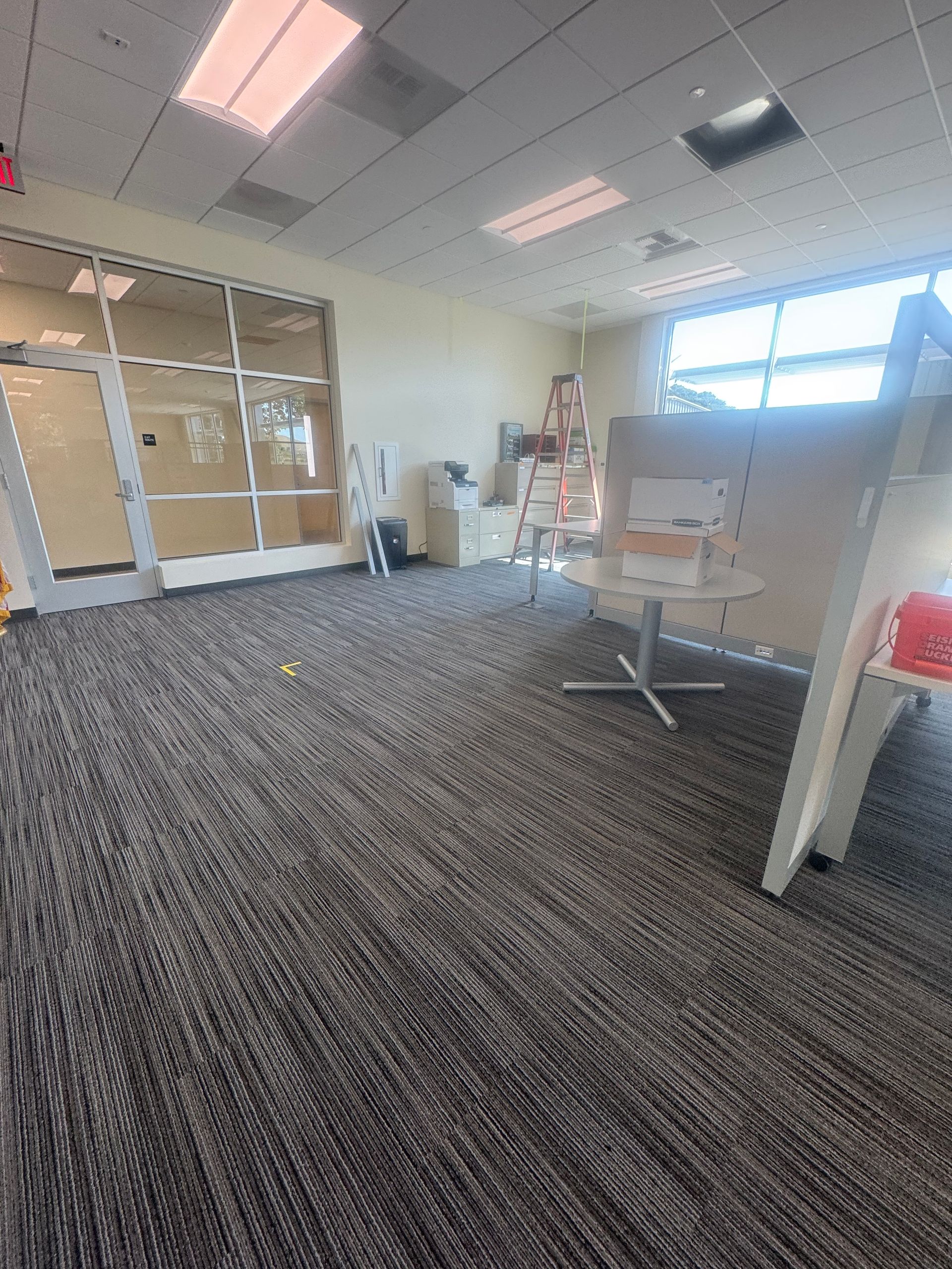 Empty office space with gray carpet, glass walls, and ladders.
