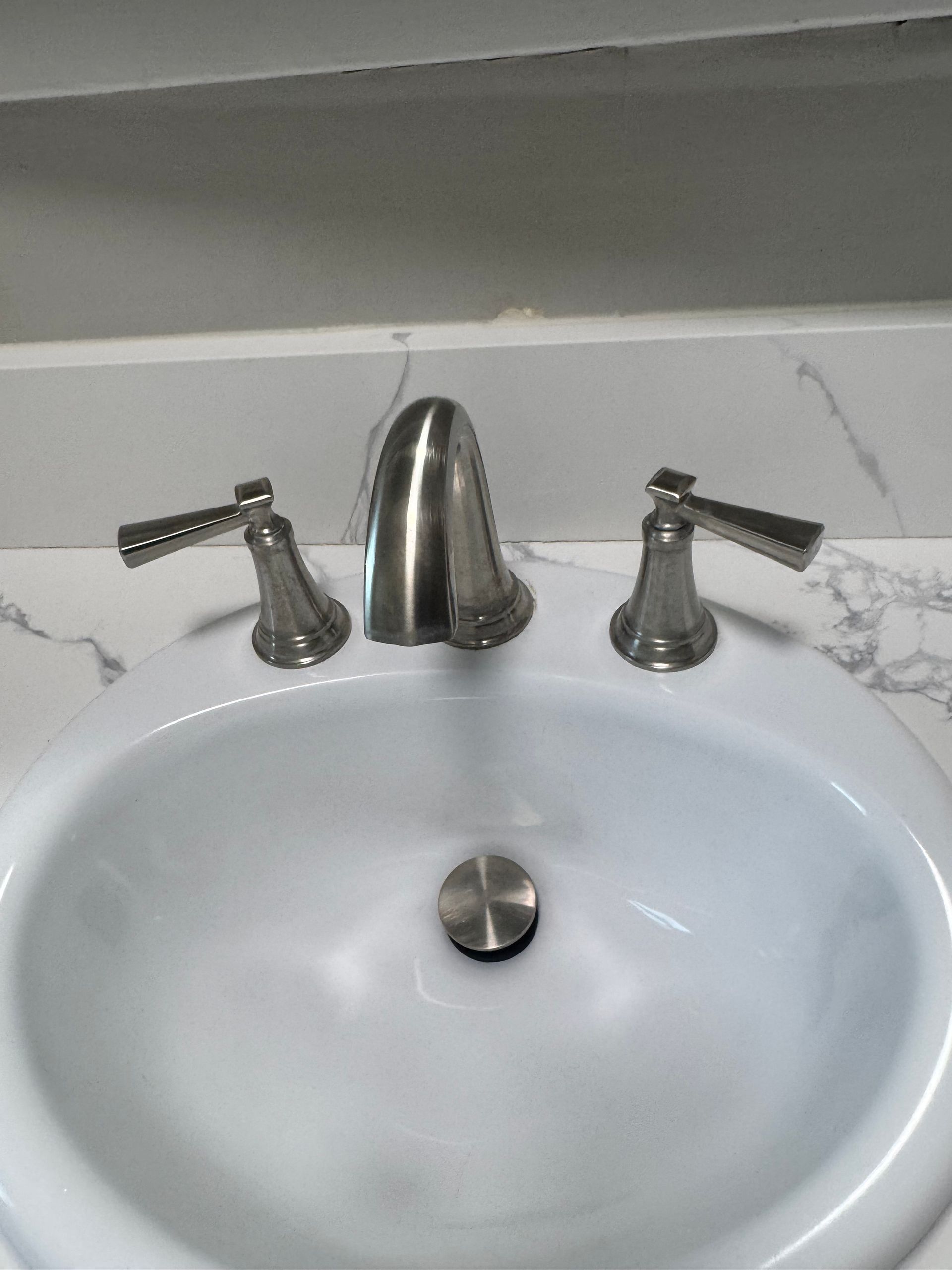 White sink with brushed nickel faucet and handles on a marble countertop.