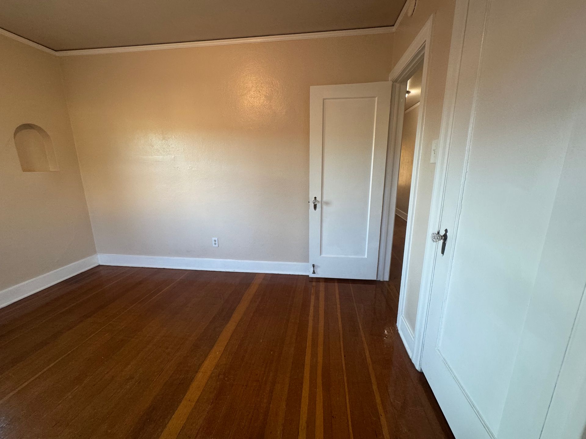 Empty room with hardwood floors, two white doors, and tan walls.