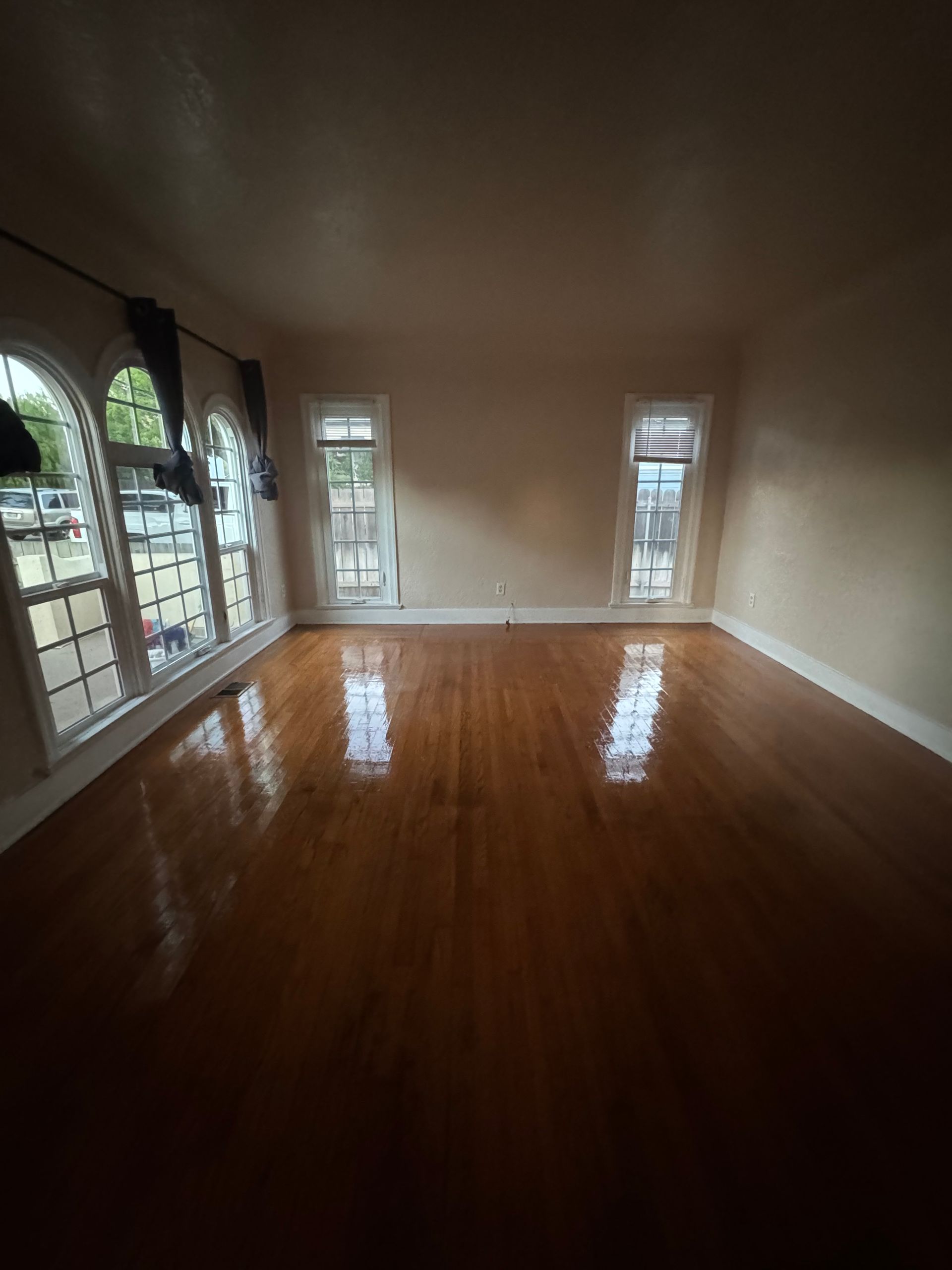 Room with hardwood floors, arched windows, and pale walls.