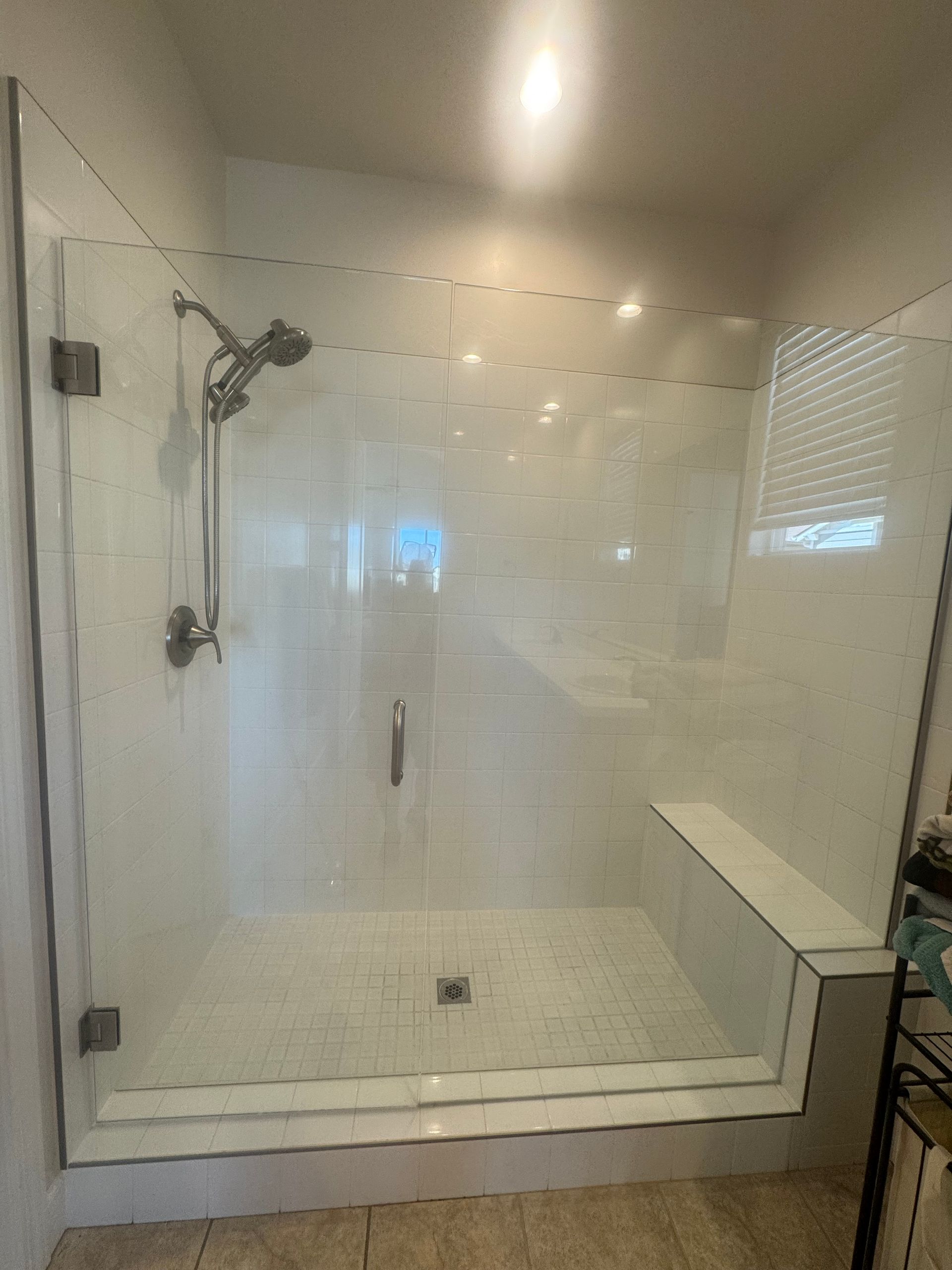 Glass shower enclosure with white tiled walls, a bench, and silver fixtures.
