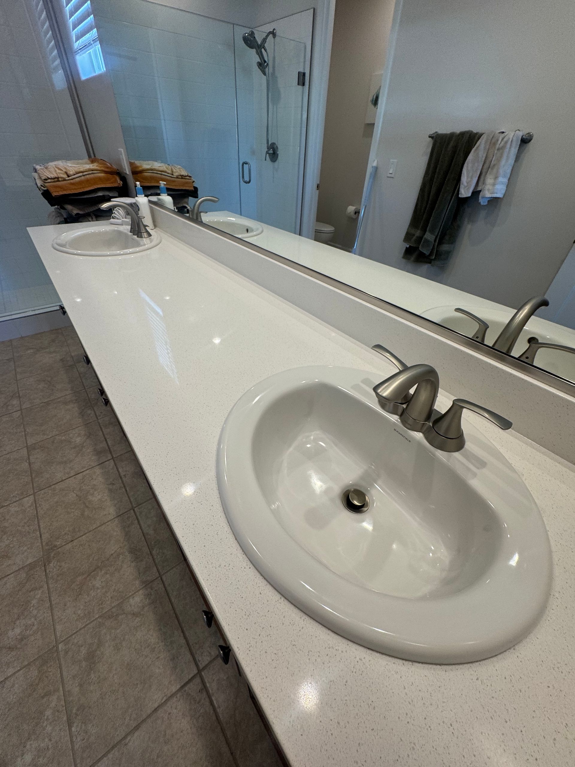 Bathroom with a white countertop, two sinks, and a long mirror.
