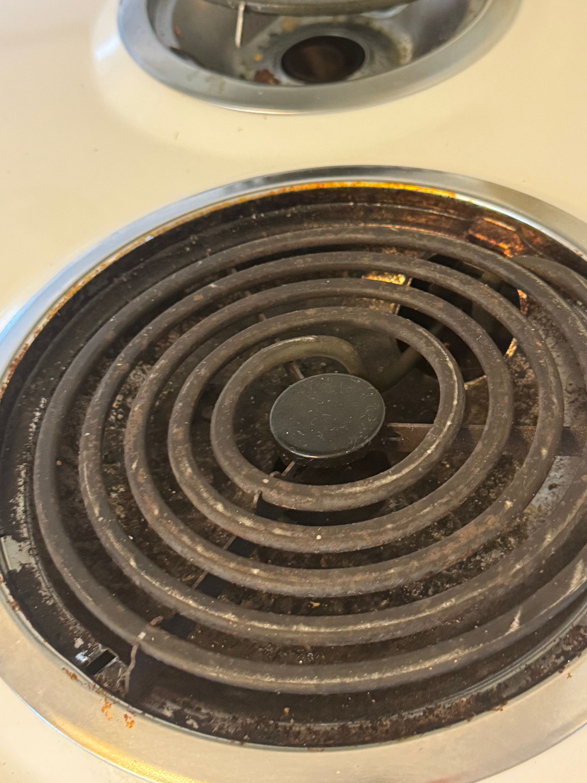 Close-up of a dirty electric stove burner coil, with a white stove top and grime buildup.