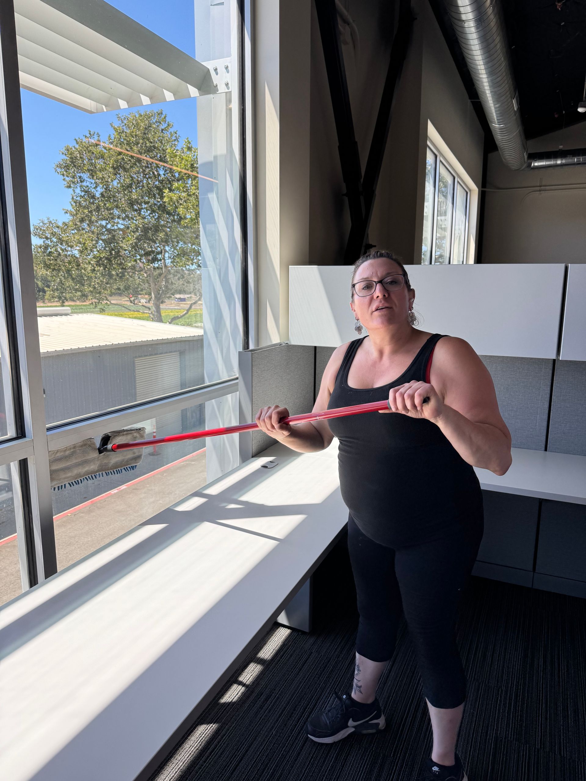 Woman in black workout clothes, using a red resistance band near a window in a bright room.