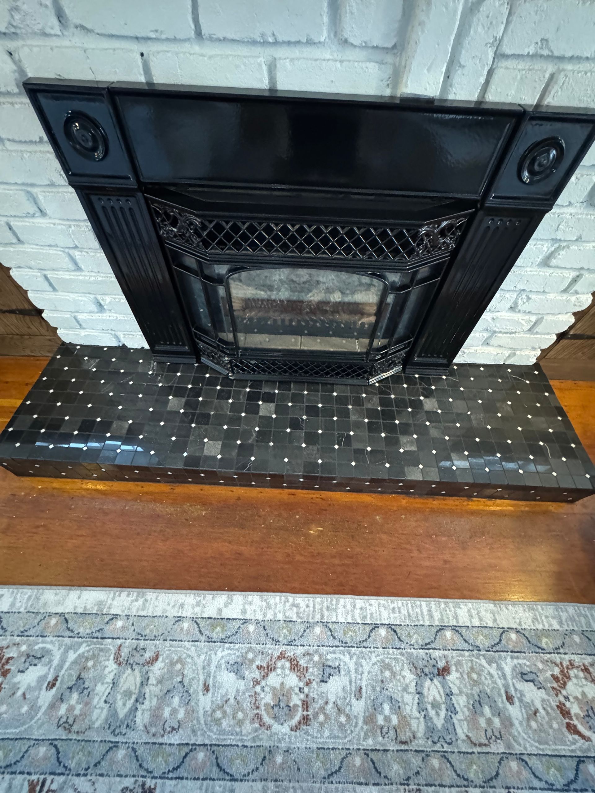 Black fireplace with tile hearth, set against white brick and wood floor.