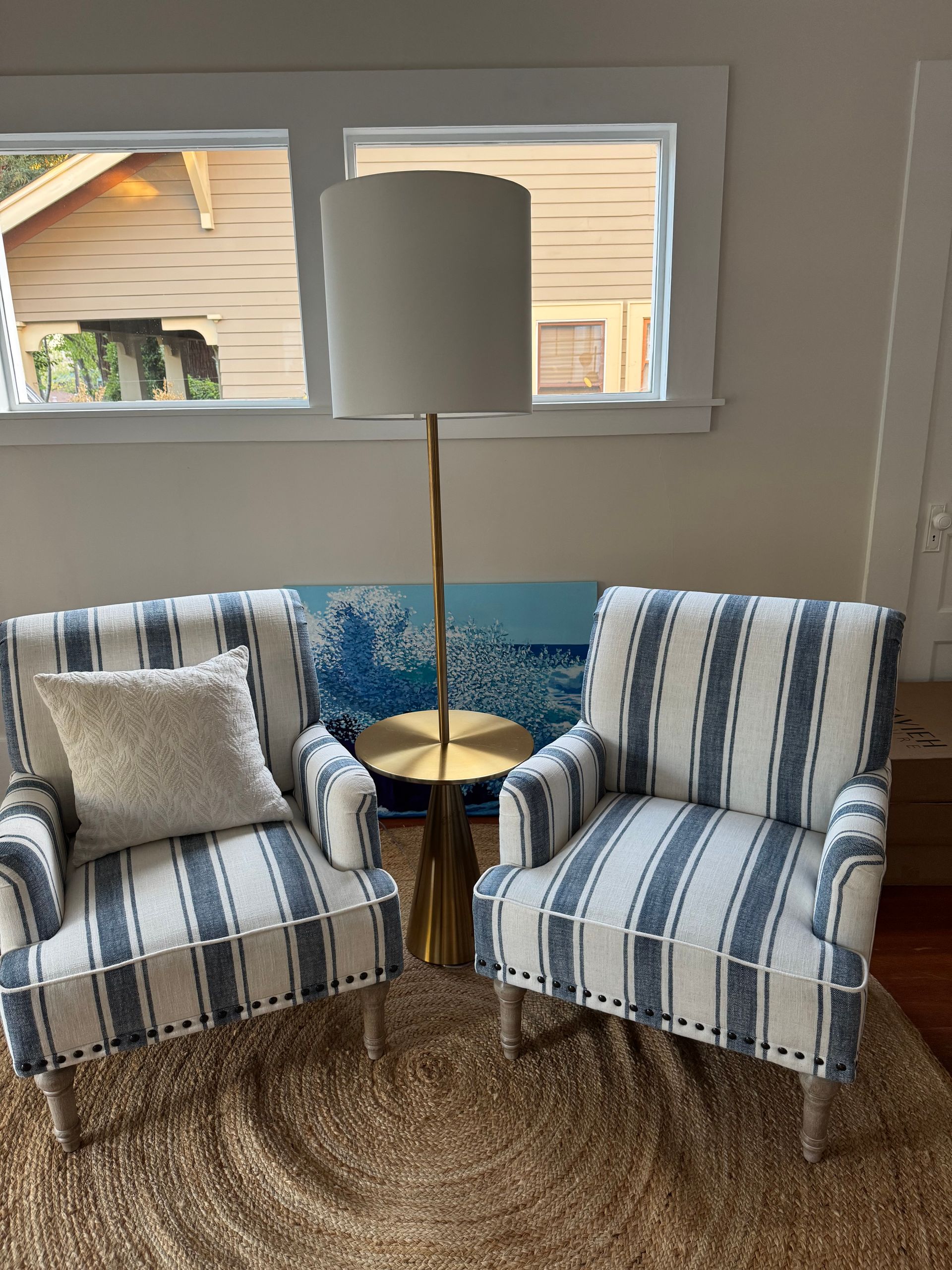 Two striped armchairs with a floor lamp and a blue wave painting.