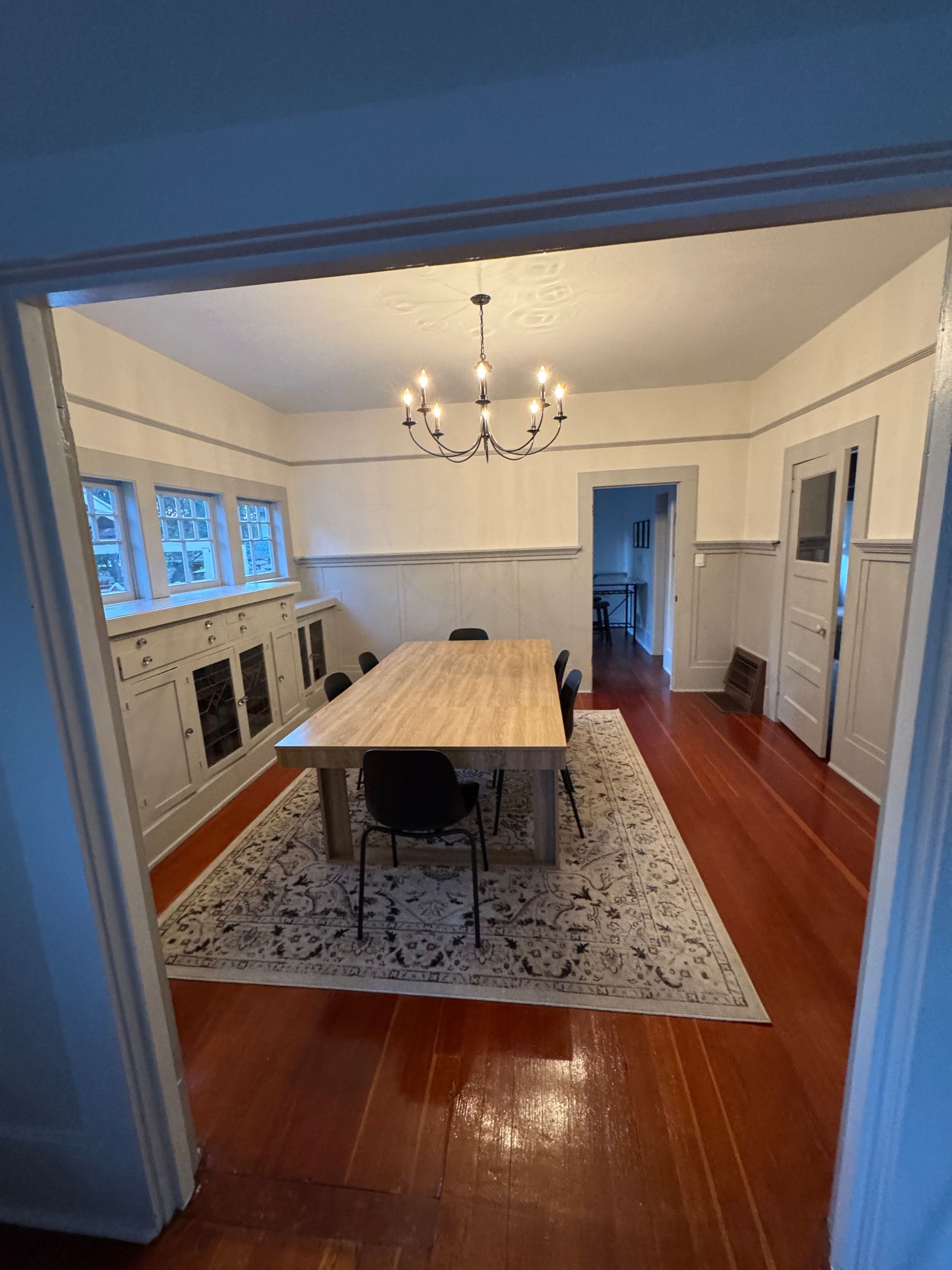 Dining room with a wooden table, chandelier, and rug on a hardwood floor.