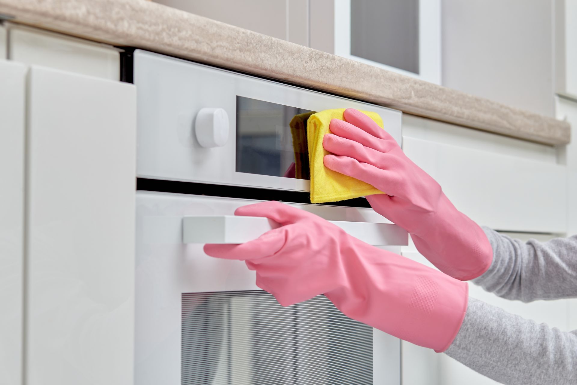 A person wearing pink rubber gloves is cleaning an oven with a yellow cloth.