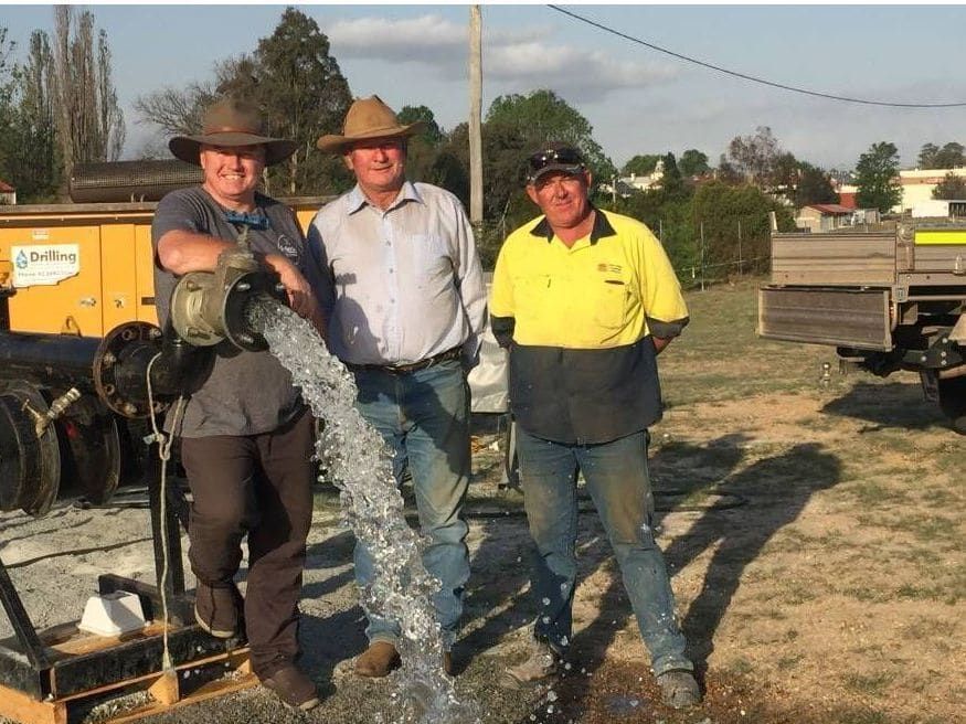 Three Men Are Standing Next To A Hose That Is Pouring Water — Water Resources Drilling In Bathurst, NSW