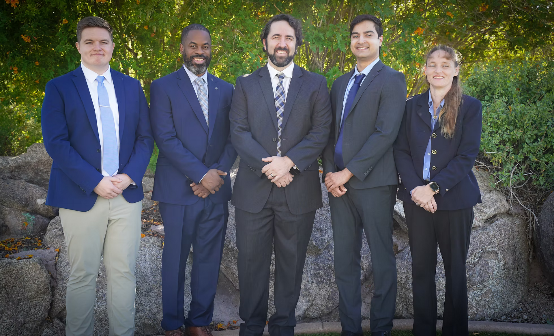 Five people in suits stand outside; smiling, arms crossed.