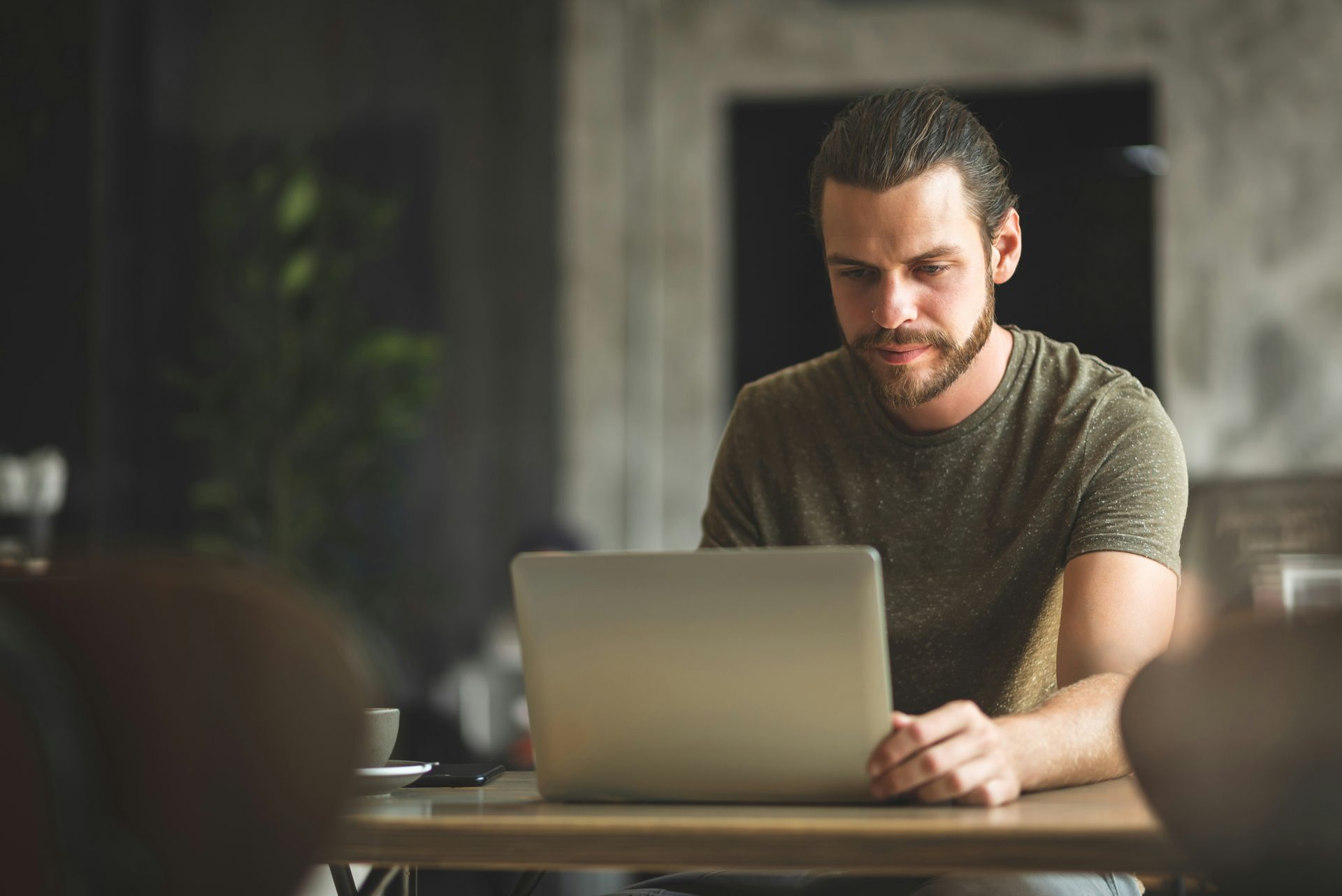 Man using a laptop at a table, likely in a cafe; looking focused.