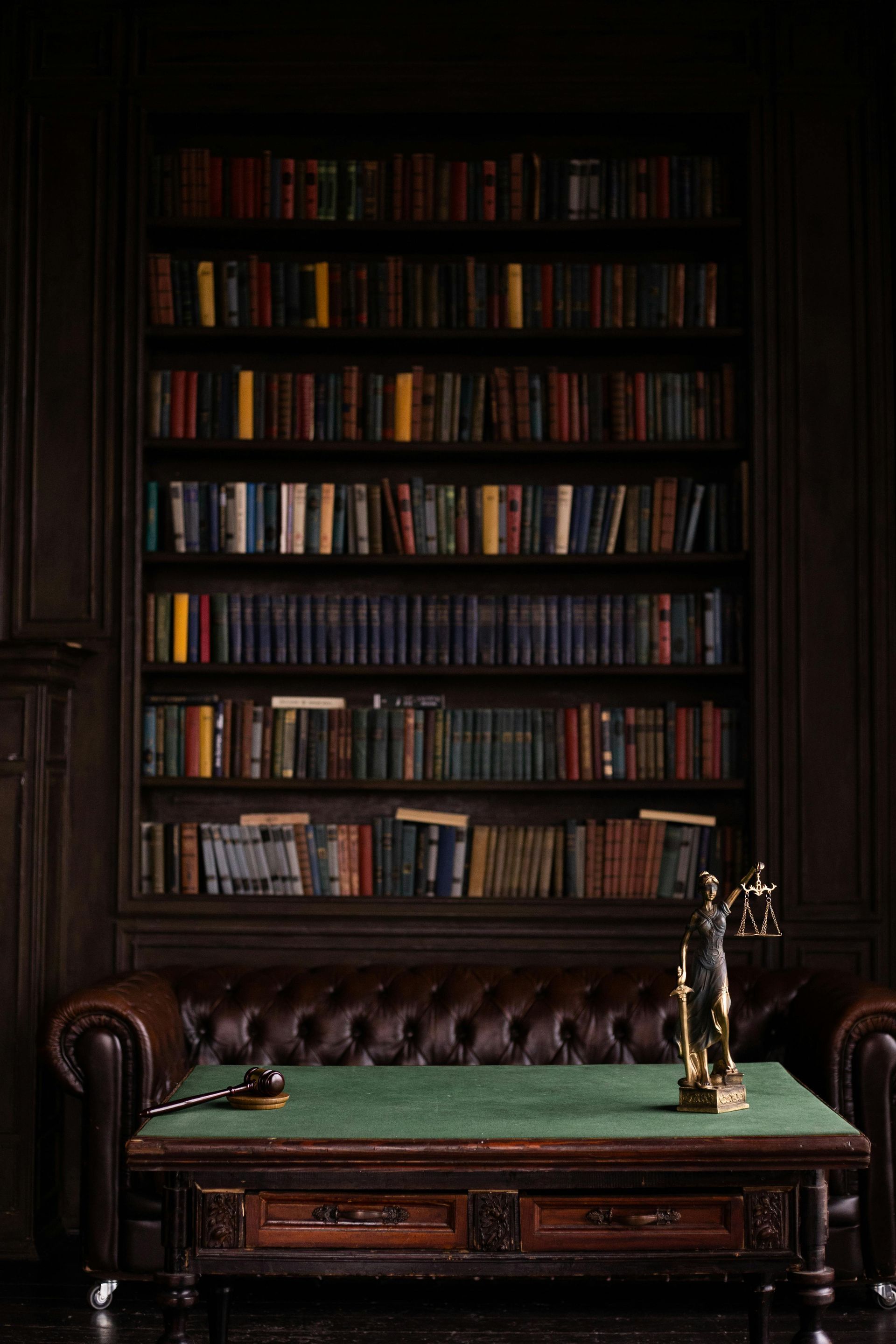 Dark library with built-in bookshelves, leather couch, green-topped table, and desk lamp.