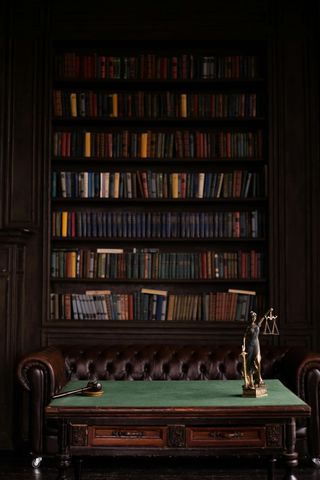 Dark library with built-in bookshelves, leather couch, green-topped table, and desk lamp.