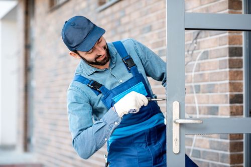 Worker in blue overalls using a key on a white door outdoors