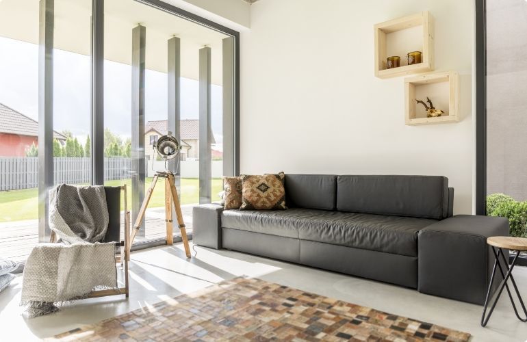 Bright modern living room with gray sofa, floor-to-ceiling windows, and a tripod by the door